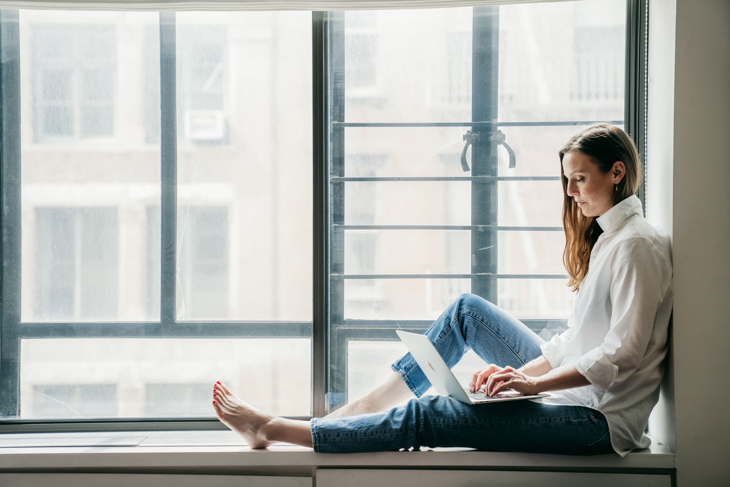 Henley Vazquez sits near the window and works on her laptop at her apartment in New York City