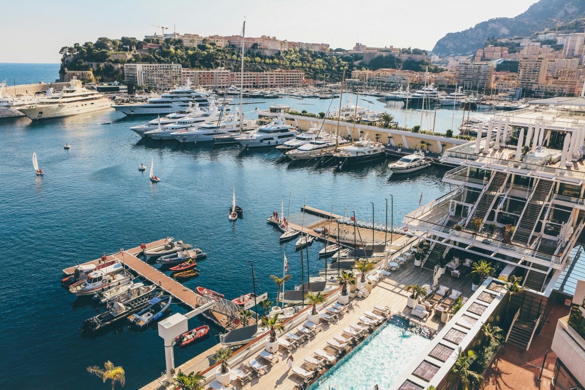 A marina in along the French Riviera that has many boats docked and a beautiful mountain scape in the distance.