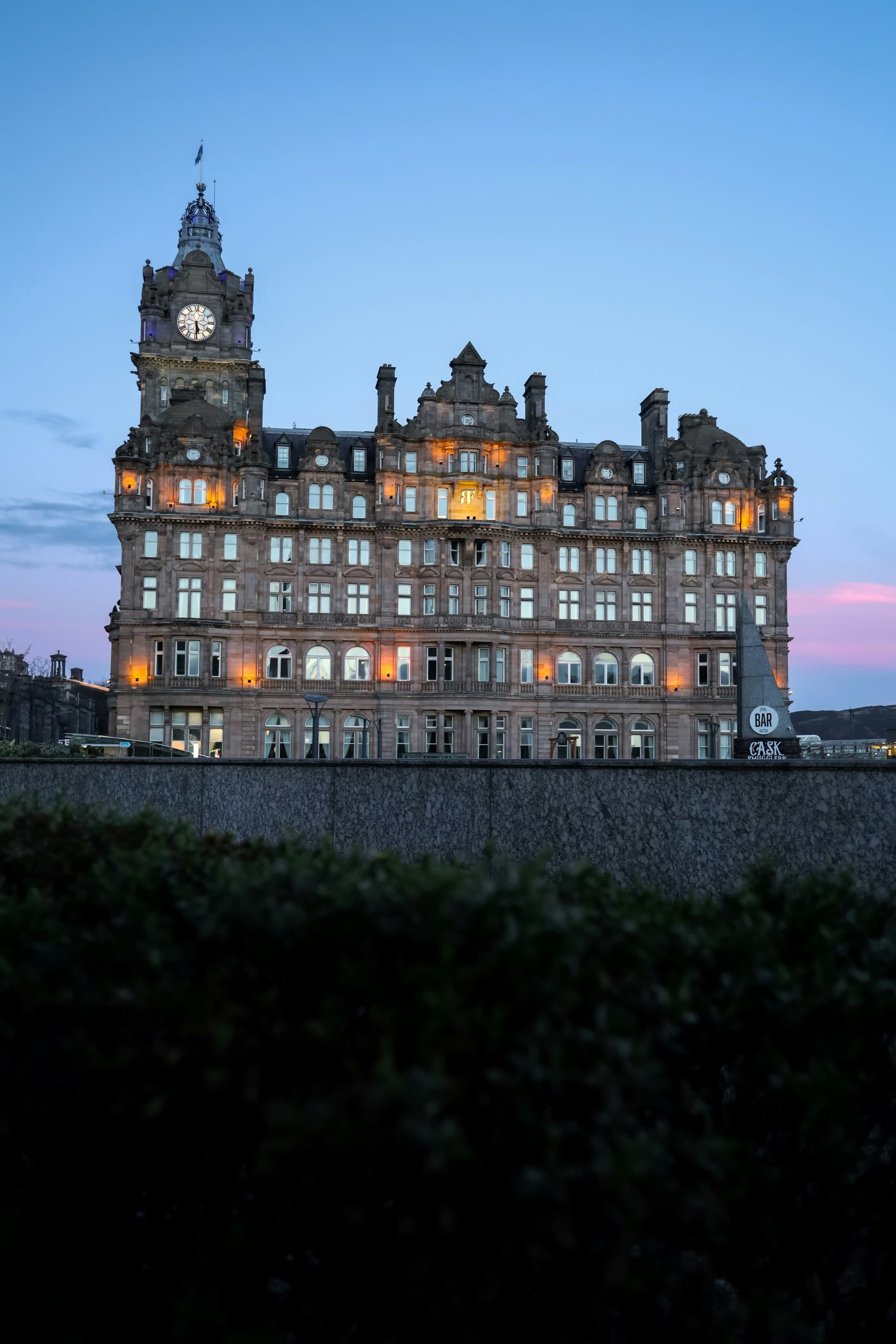 A grand hotel lit up against the fading blue and pinks of the sky at dusk.
