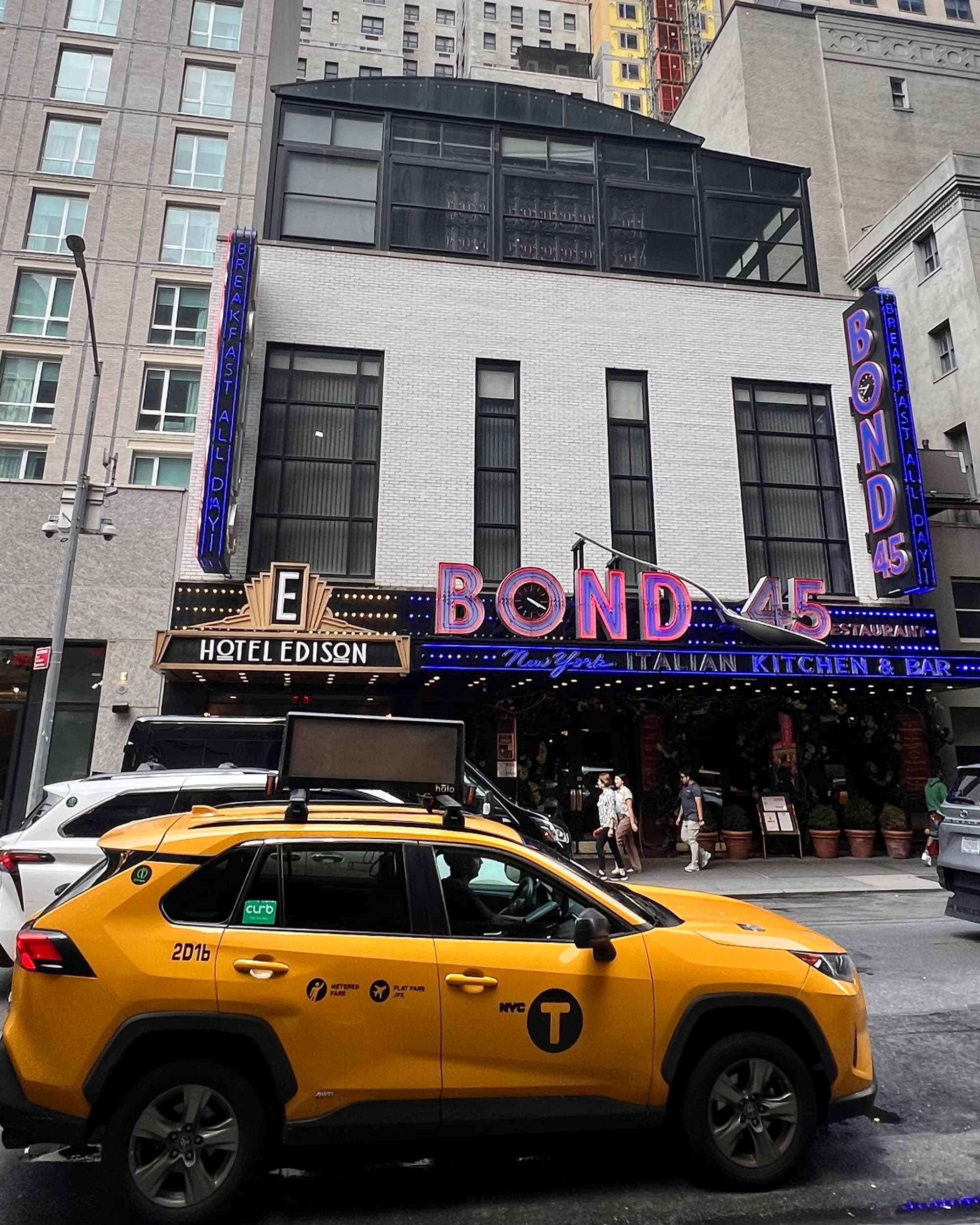 Exterior of a hotel on a busy New York street with a yellow taxi cab in the foreground.