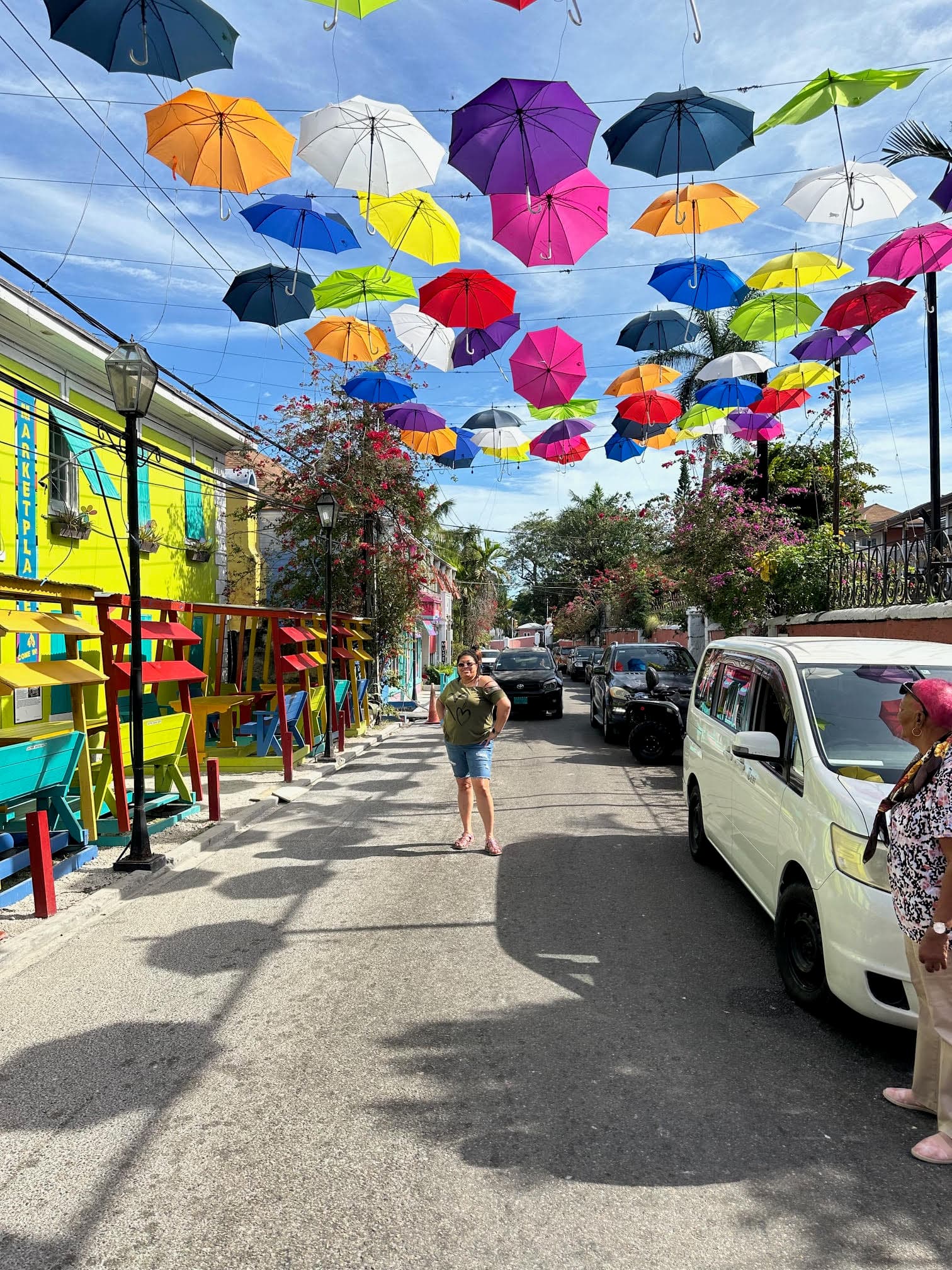 A person standing under a group of hanging, multicolored umbrellas above a street, posing for a photograph