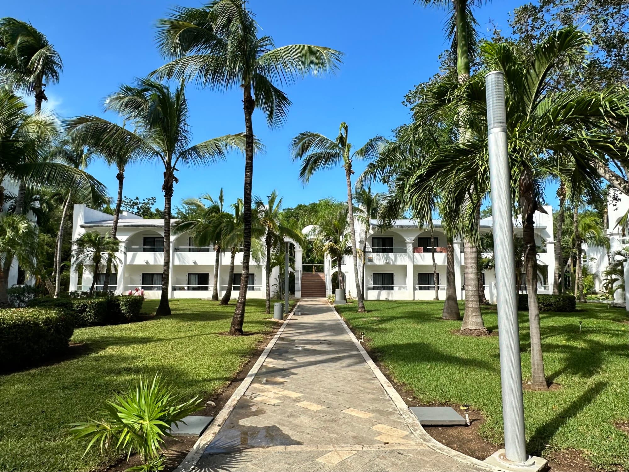 Outside view of a hotel building with a brick pathway leading to us surrounded by palm trees