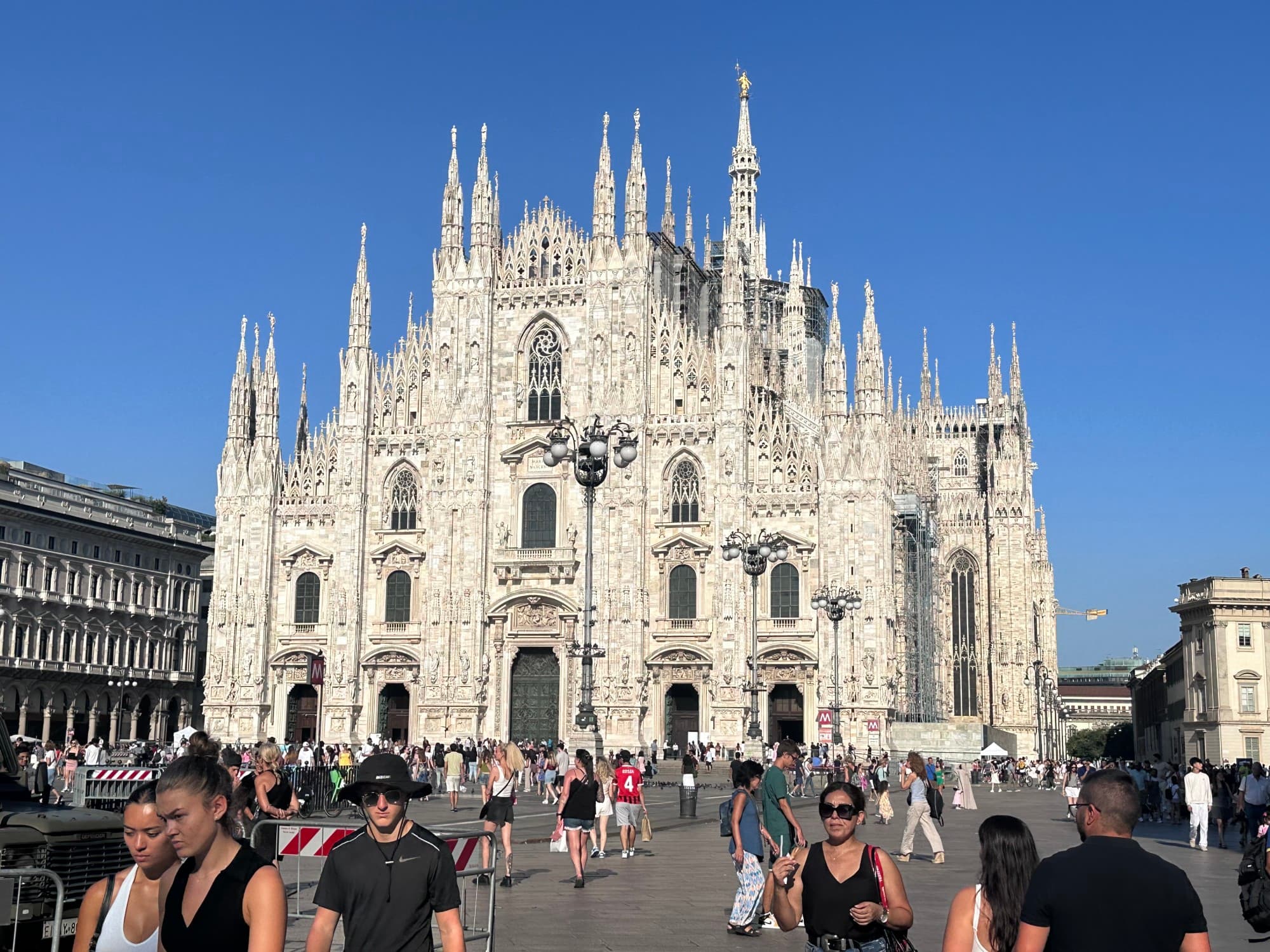 Exterior of a Gothic-style cathedral made of white stone with a busy plaza of people in front.
