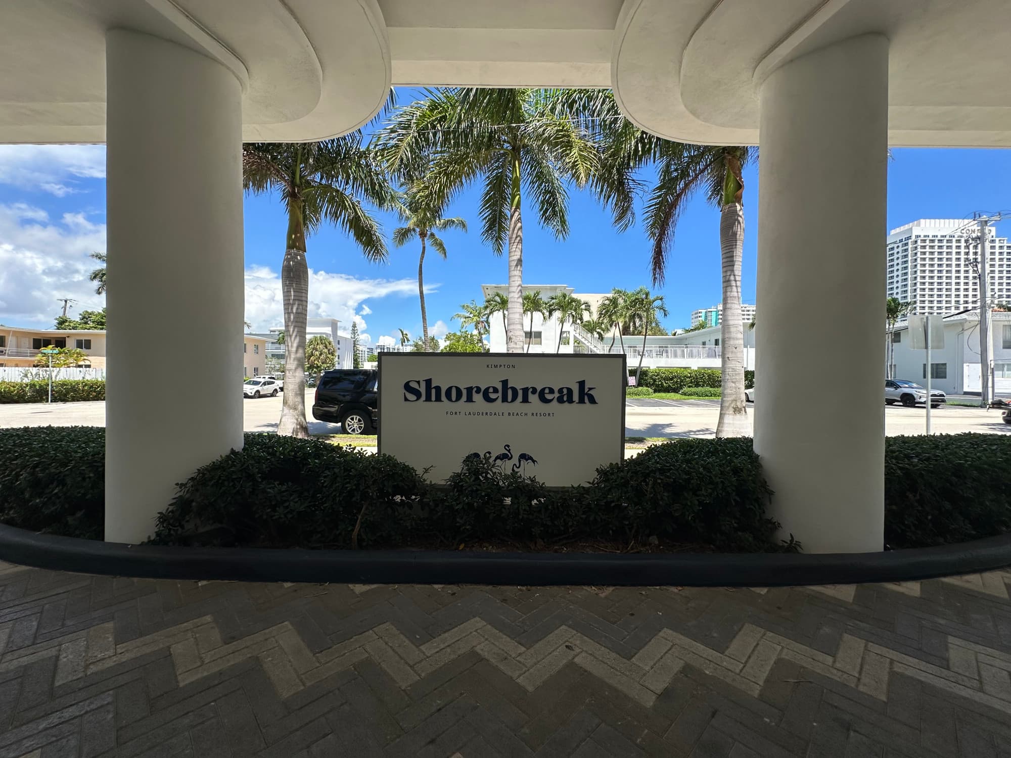 A sign in front of palm trees outside reading "Shorebreak"