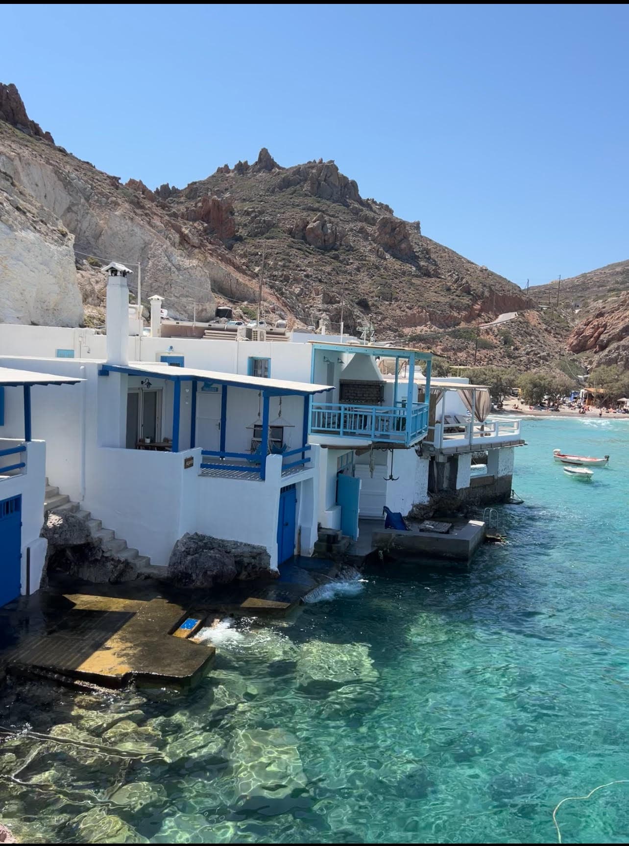A view of traditional white and blue houses looking out to crystal-clear turquose waters in Greece.