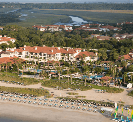 An aerial view of the island, the resort consists of many large buildings along the beach and a large pool and palm trees.