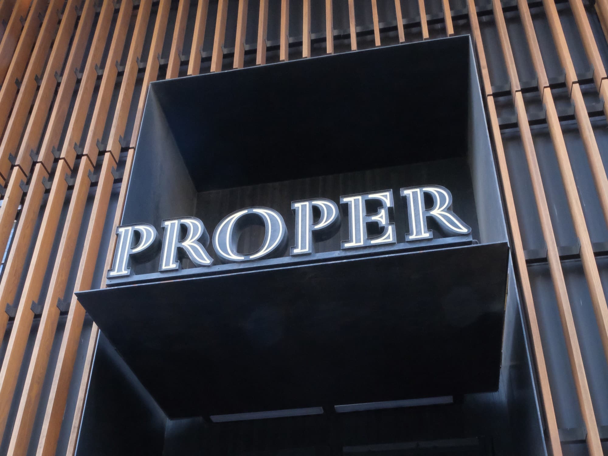 The grand entrance to Austin Proper Hotel with a neon sign surrounded by wood design.