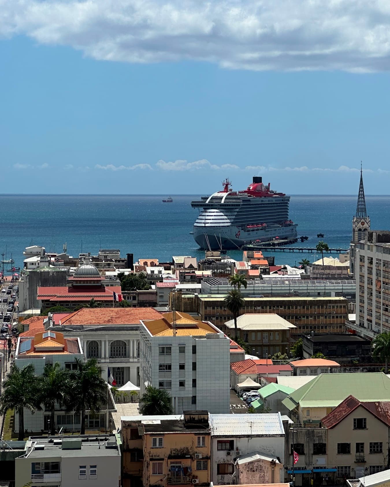 A view from a balcony overlooking the city, the ocean and a cruise ship pulling into dock.