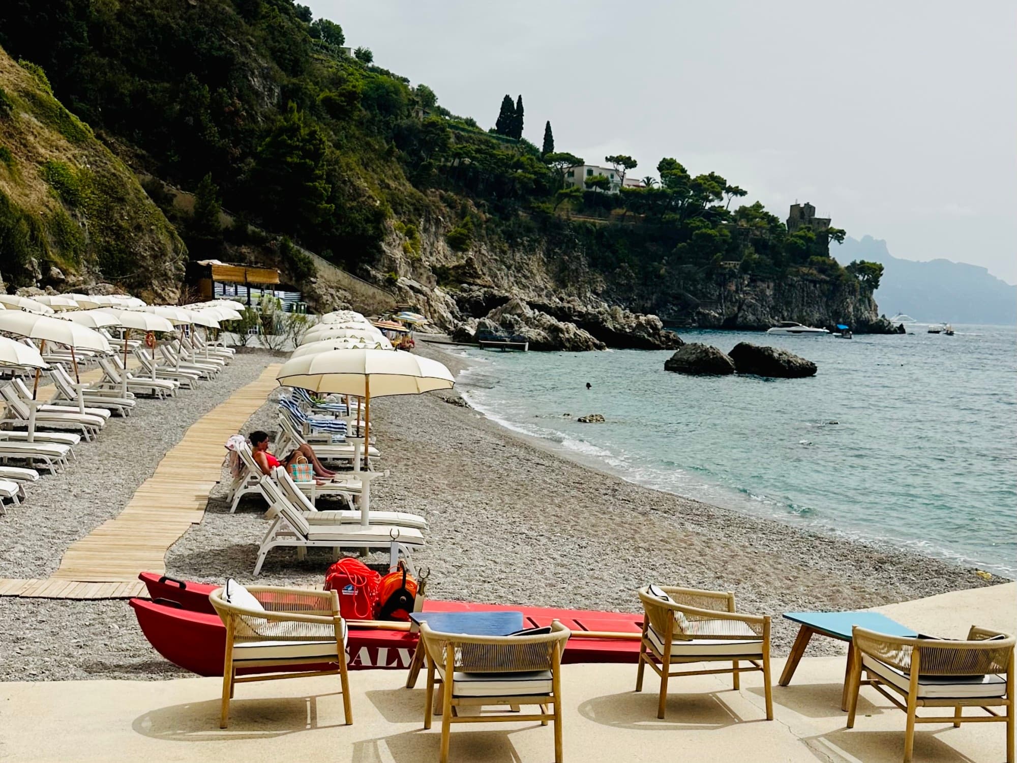 Borgo Sant'Andrea Beach Club on the Amalfi Coast boasts a pristine beach with loungers and umbrellas lining the shore overlooking clear waters on a sunny day.