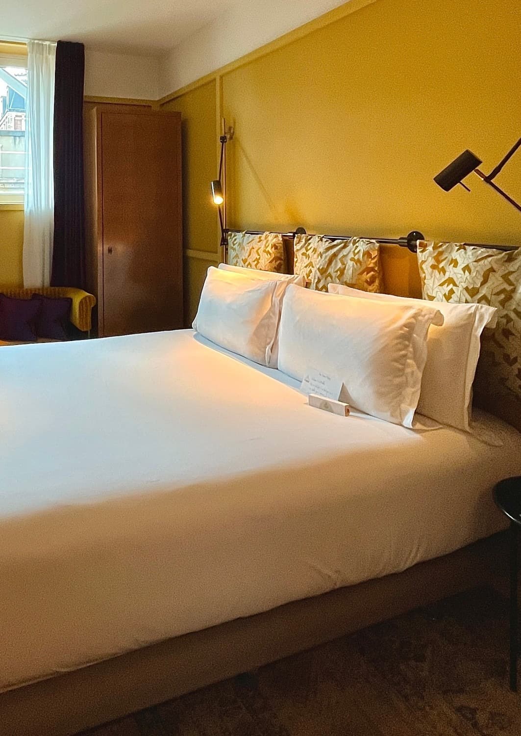 Hotel room with yellow walls and a big bed with white linens.