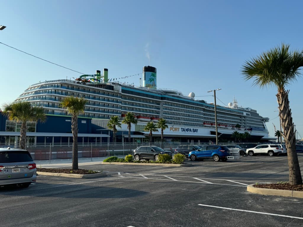 A large cruise ship docked at a port with a parking lot next to it during the daytime