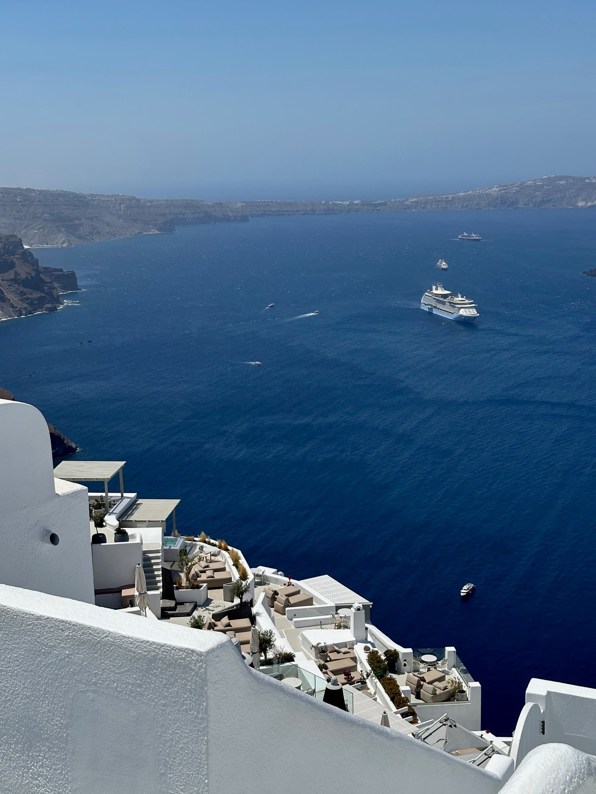 A boat in the ocean off the coast of Santorini with white buildings. - Kristyne Wada
