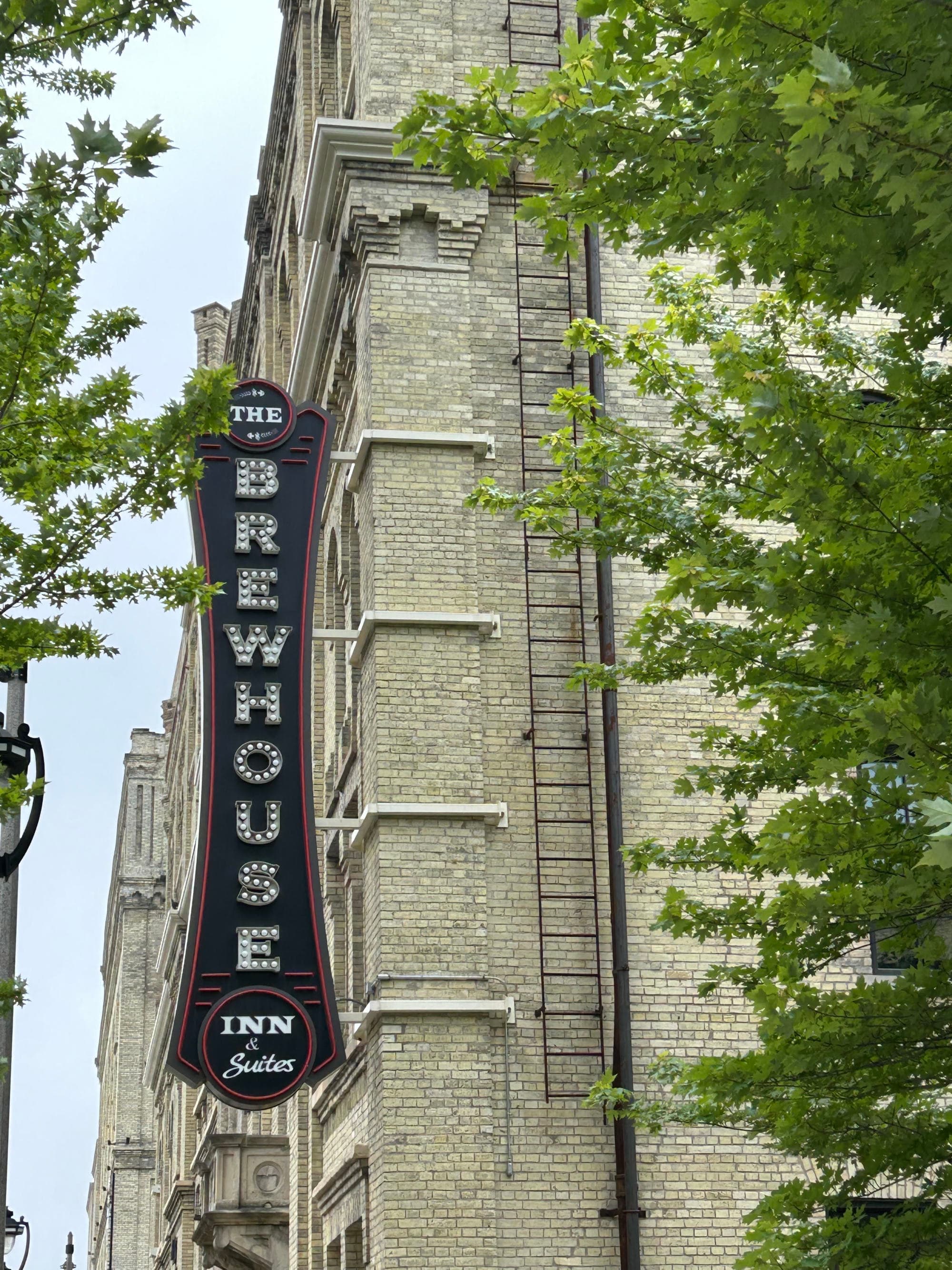 The Brewhouse Inn sign against a brick building surrounded by green foliage on a cloudy day.