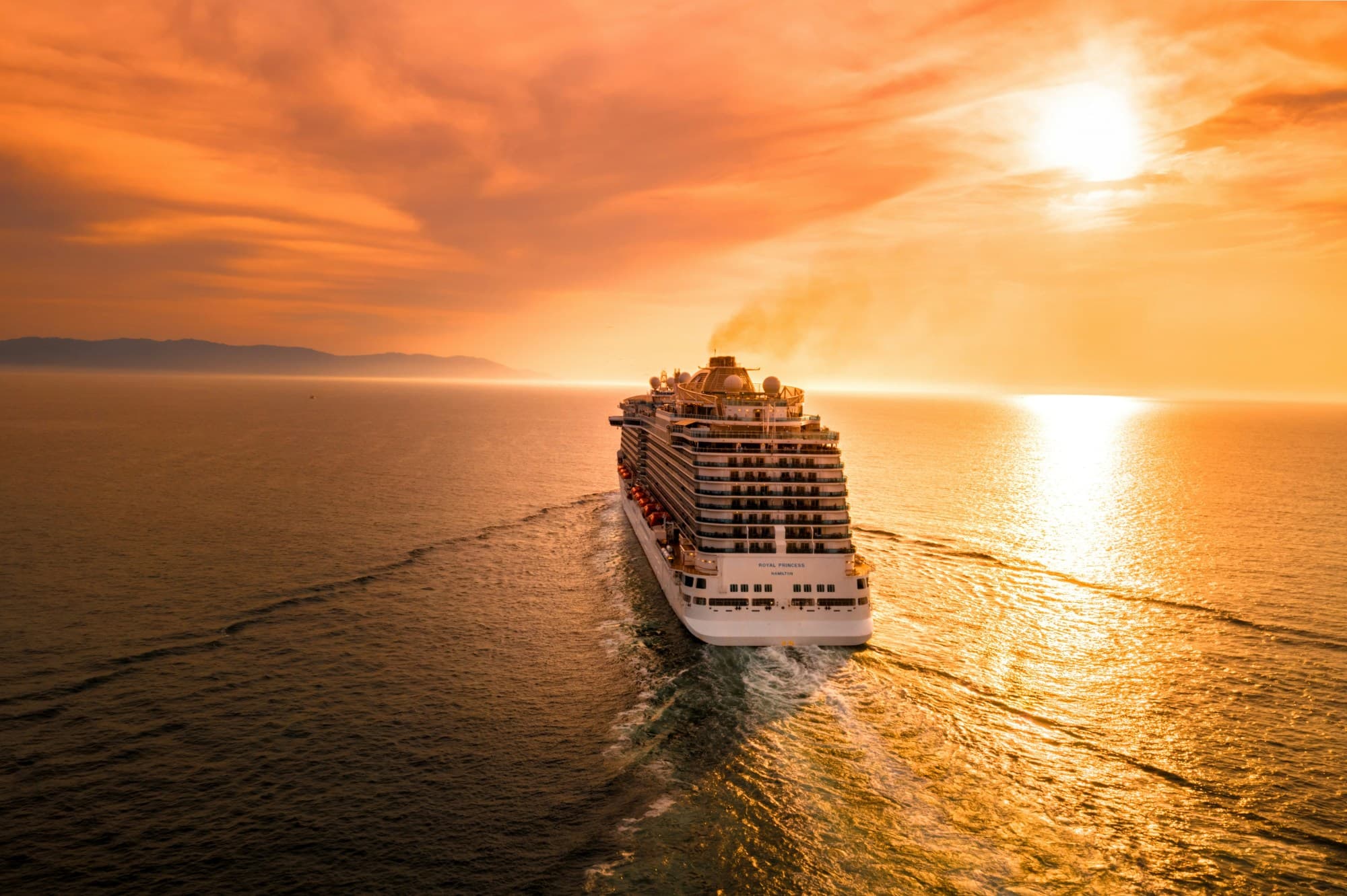 View of the cruise ship sailing towards the sunset on calm water.