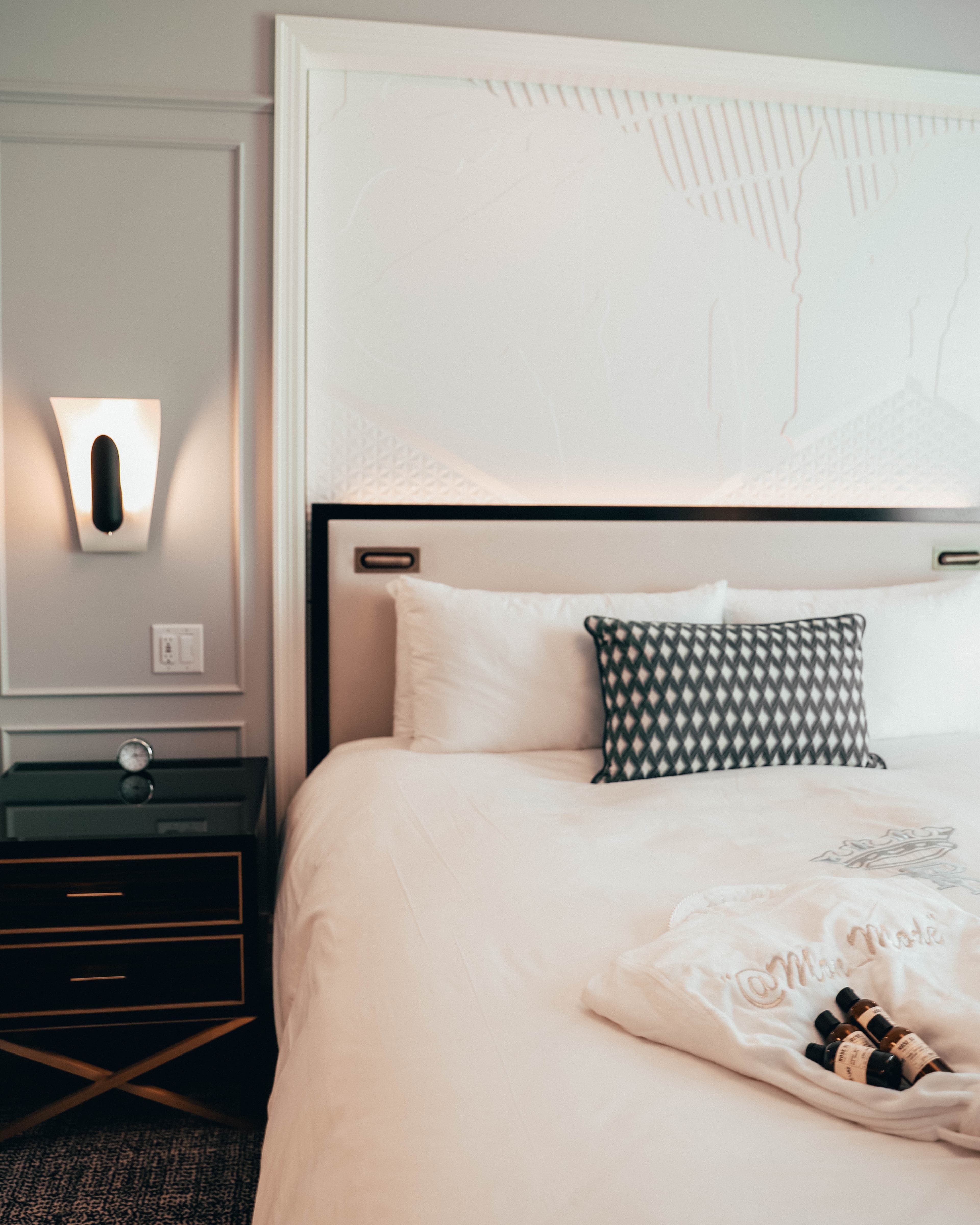 The interior of an elegant hotel room with white bedding and white and gray walls.