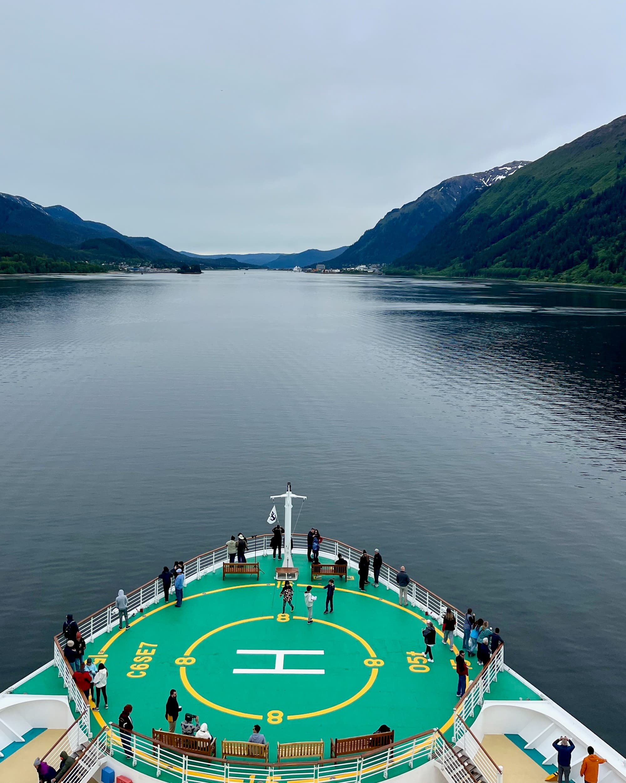 Front deck of a cruise ship on gray waters with high cliffs in the background.
