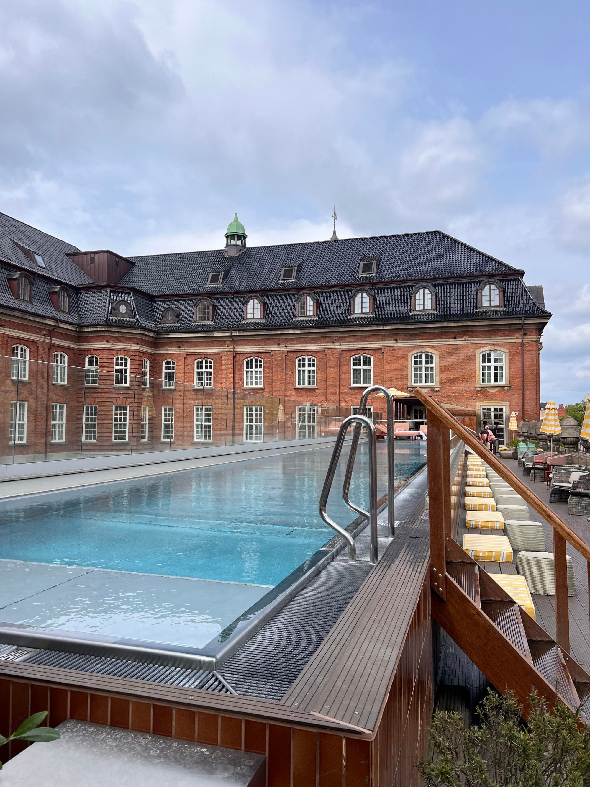 An outside swimming pool during the daytime with a red brick building in the background