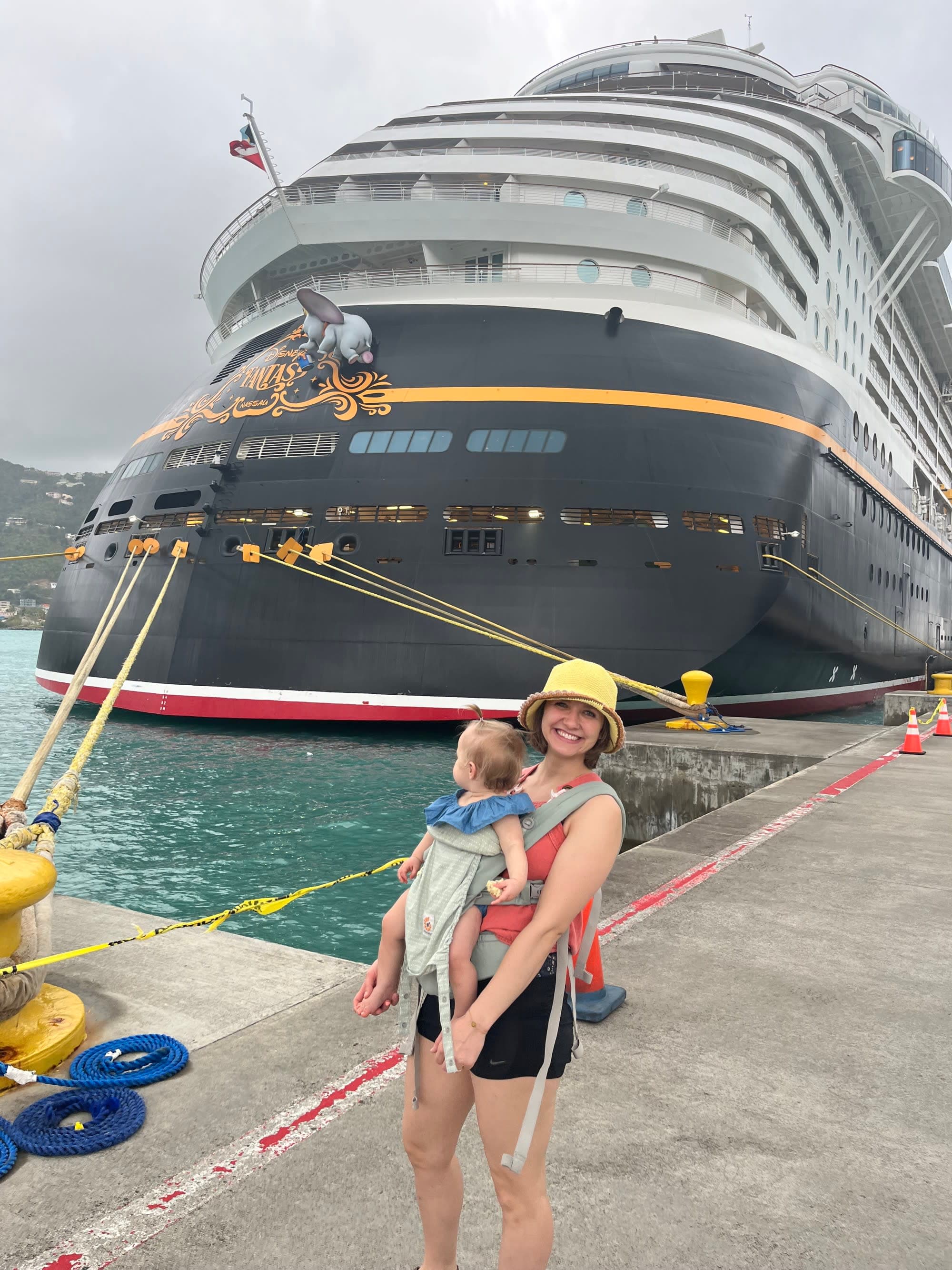 Travel advisor and baby posing before the Disney Cruise Ship at port on a cloudy day.