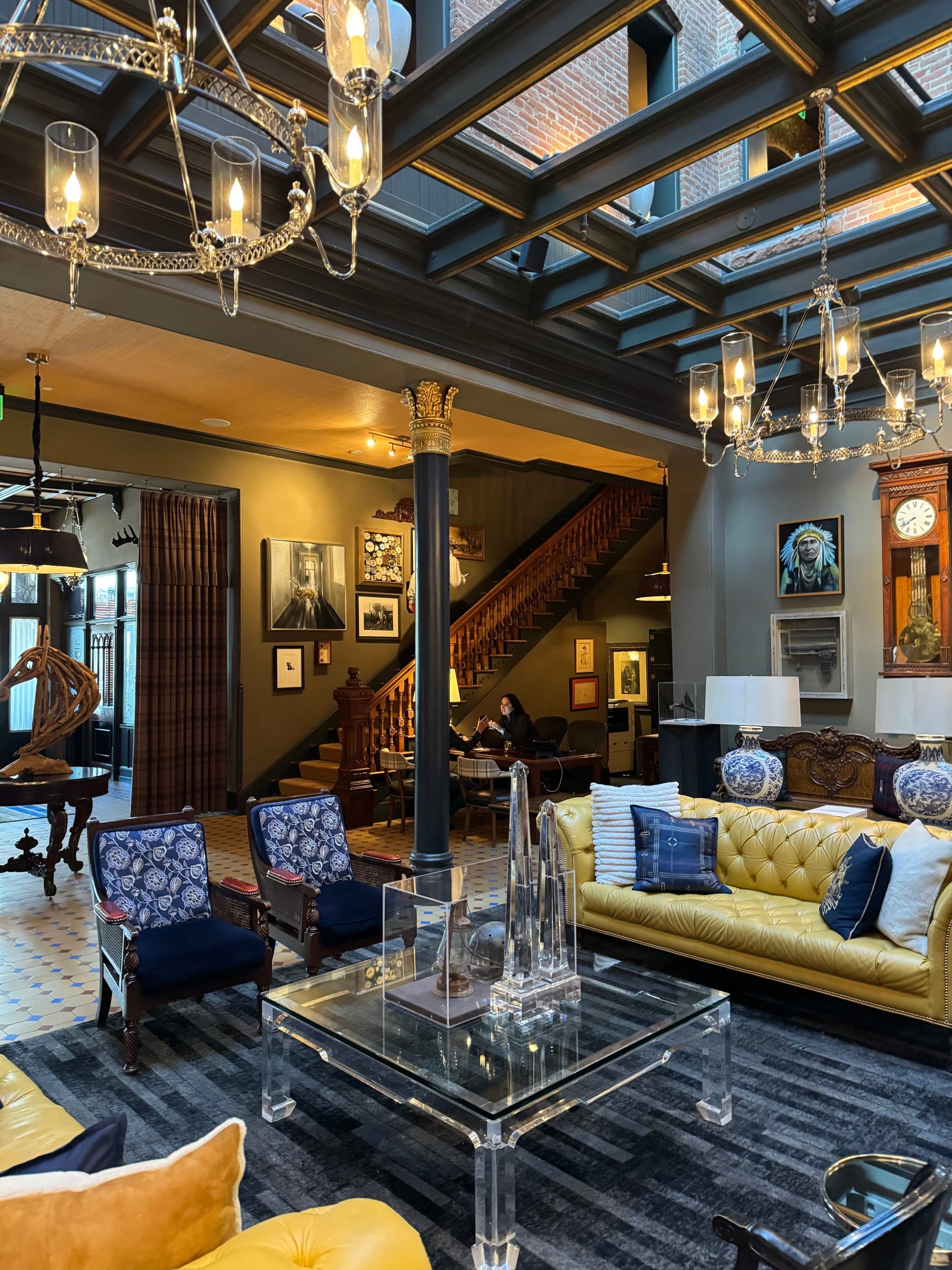 Inside the lobby of the Hotel Jerome, with luxurious couches, sitting chairs, decor, light fixtures and a glass ceiling.