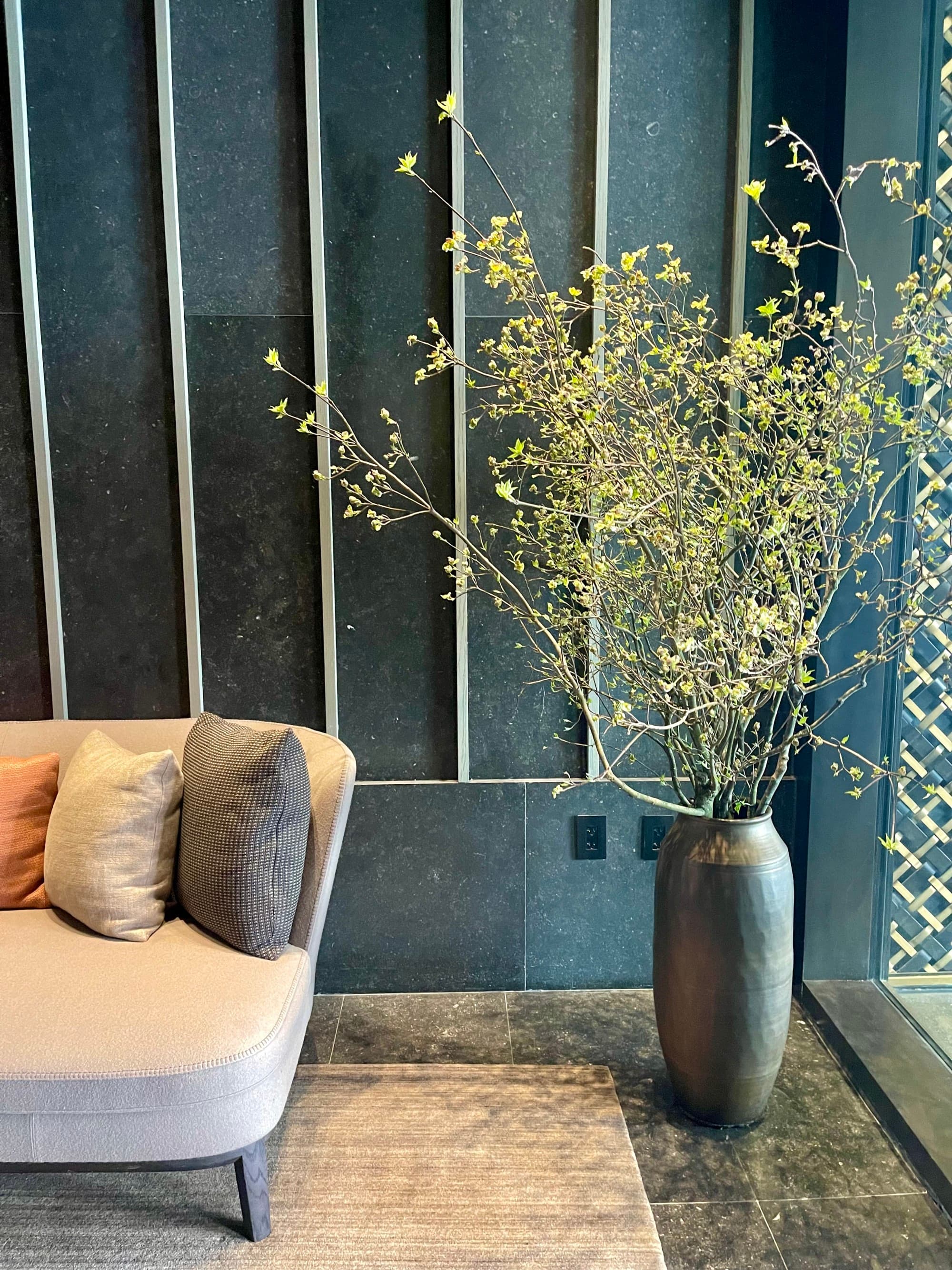 Inside the hotel, showcasing room details, such as a couch with pillows and a plant in a silver vase.