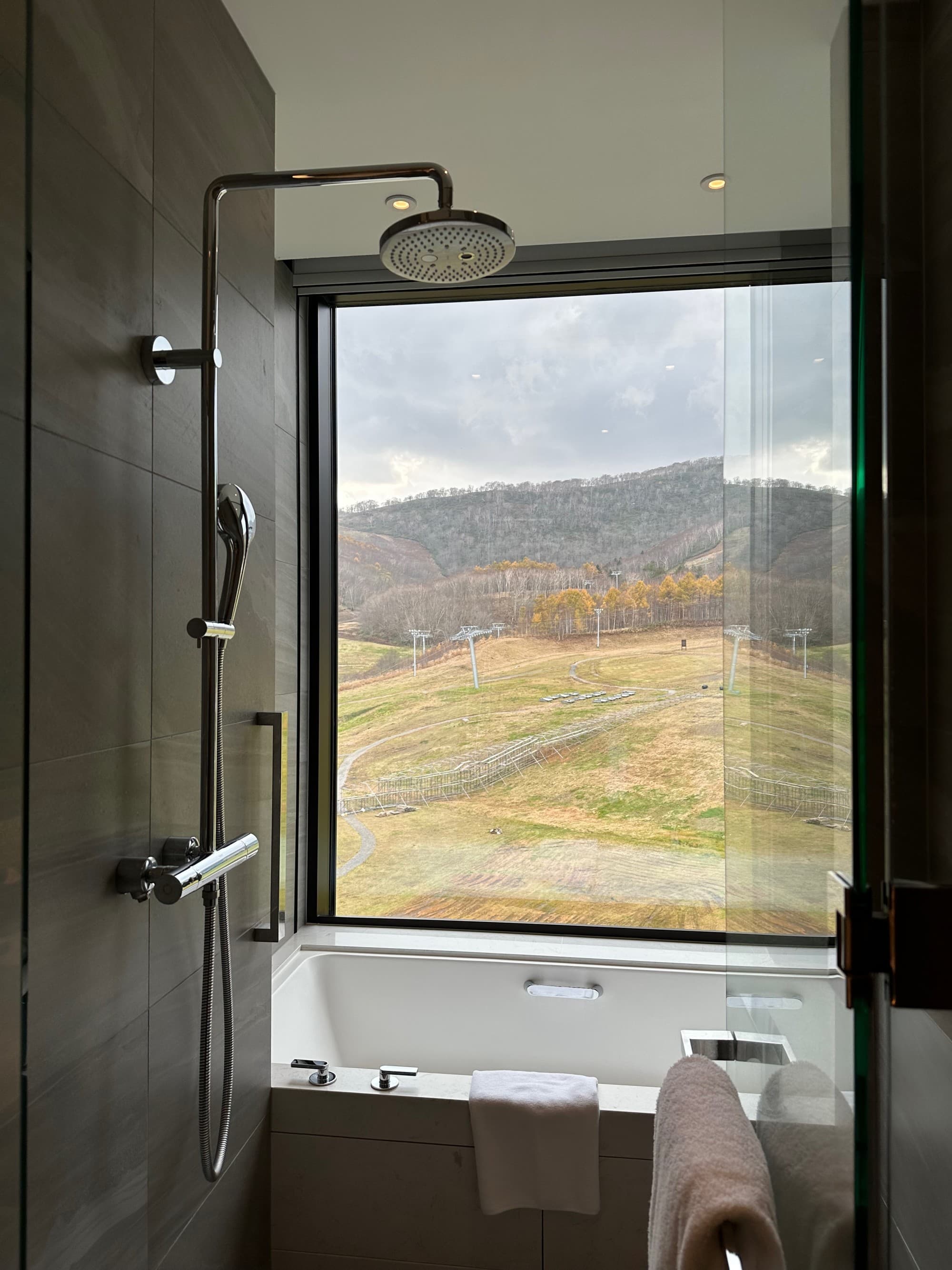 A bathroom at the Park Hyatt Niseko with a shower and view of the countryside with fall foliage