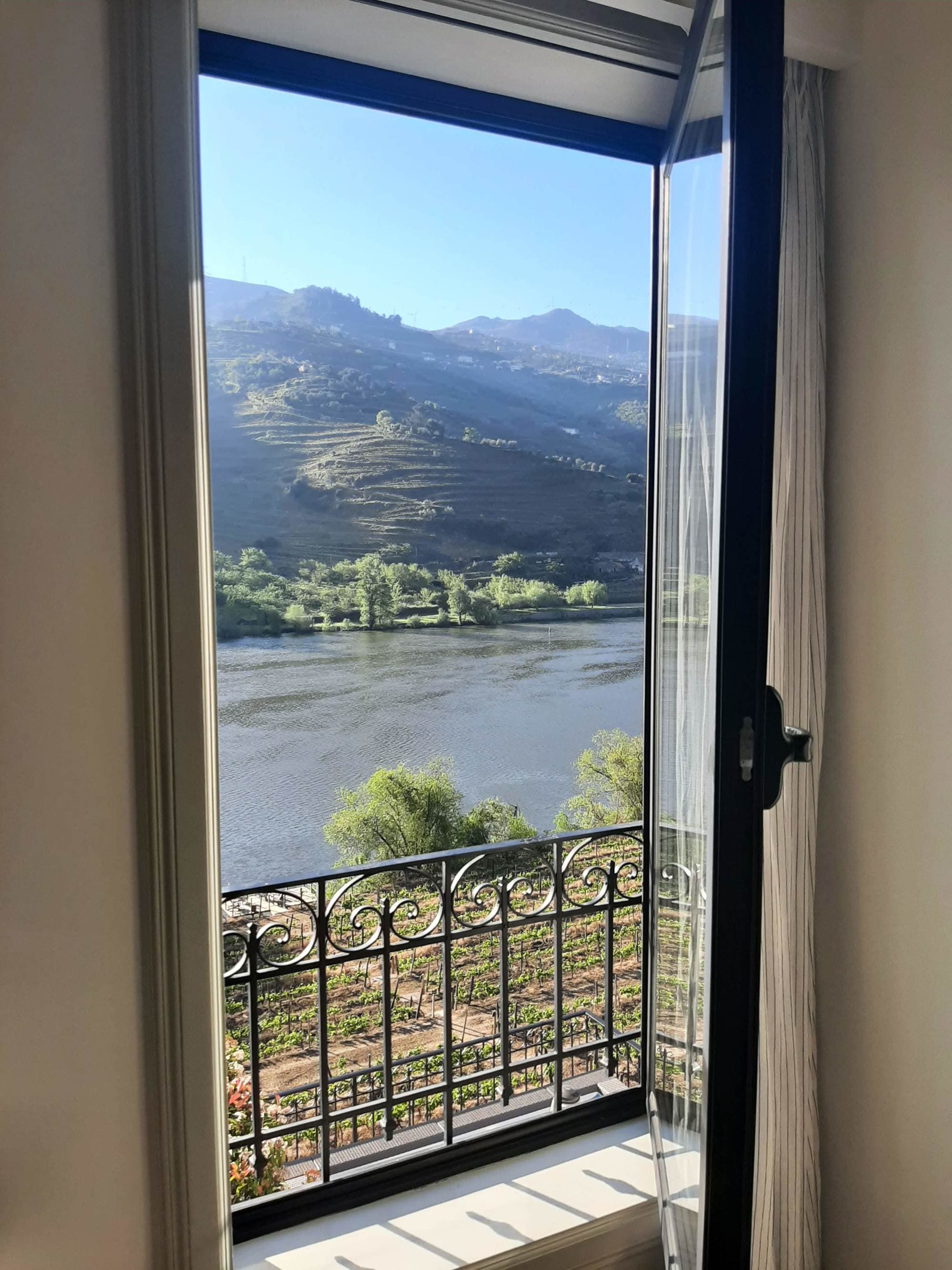 A view of a lake and mountains on a sunny day from inside a hotel room, through an open door.