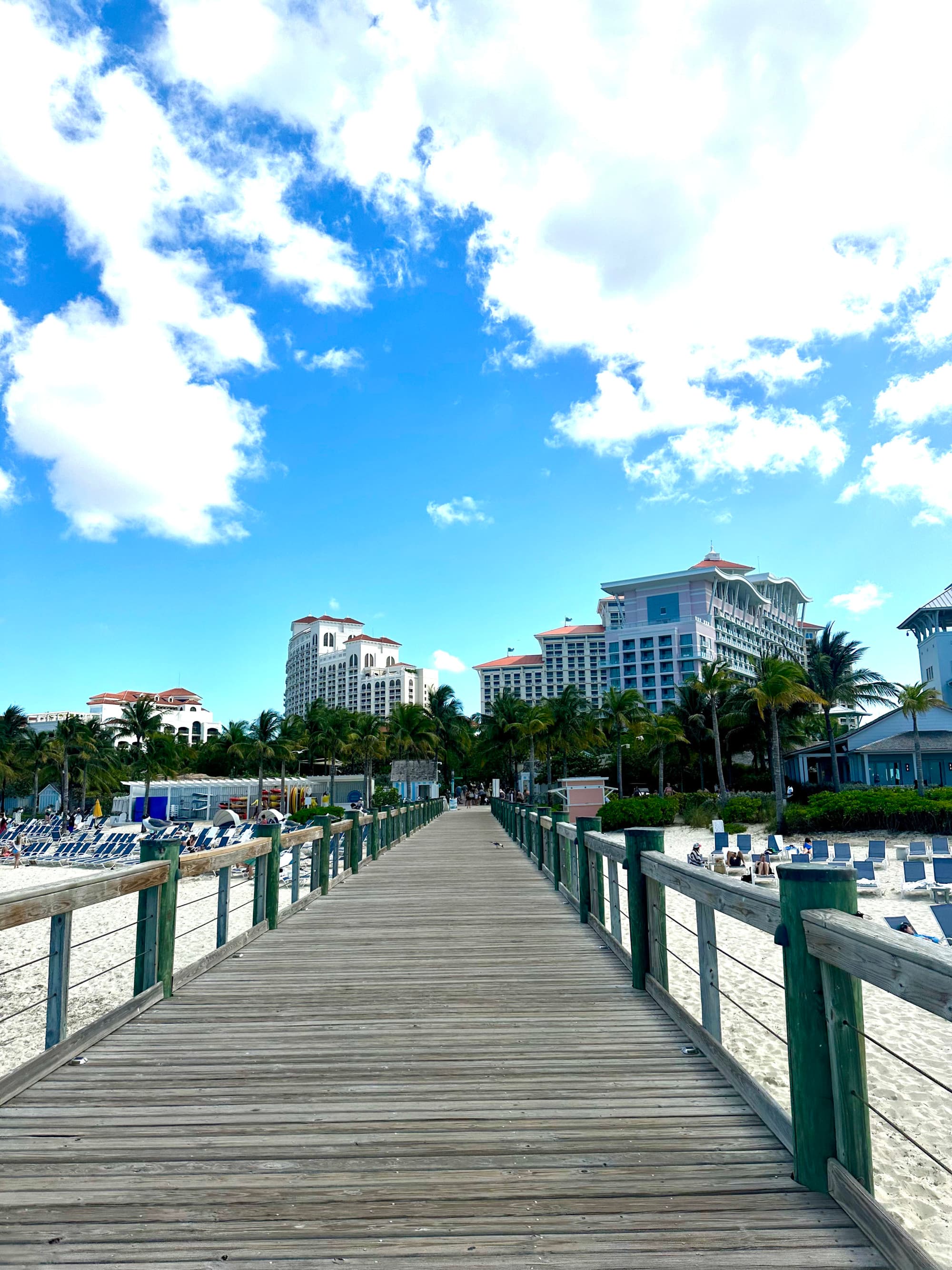 A point of view shot from a pier leading to the sandy shores before Baha Mar Hotel on a sunny day.