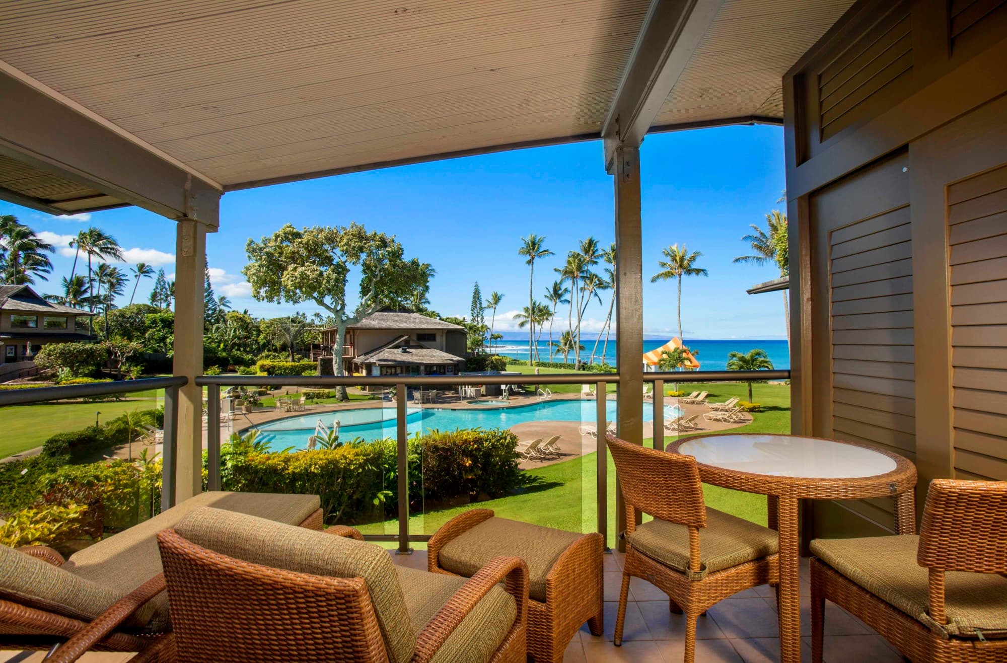 A hotel patio with furniture looking out on a green lawn and palm trees