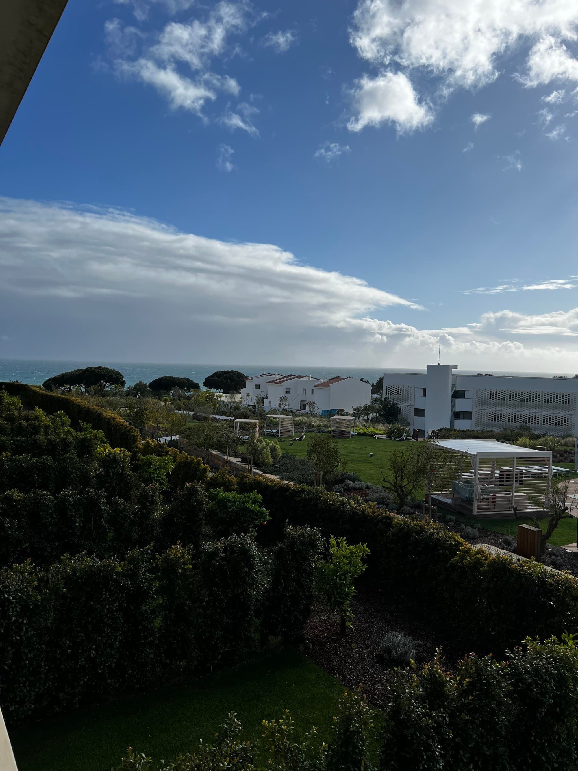 View out a hotel window of green trees and white houses beside the sea