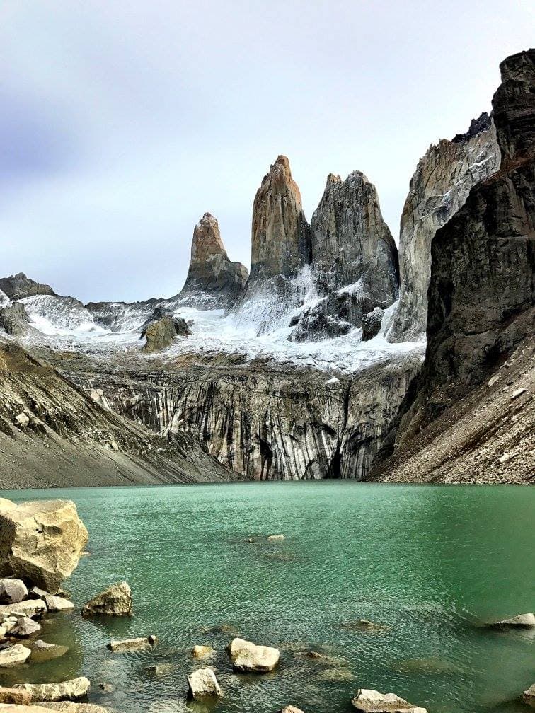 A crater lake surrounded by large rock formations, that are sprinkled snow.