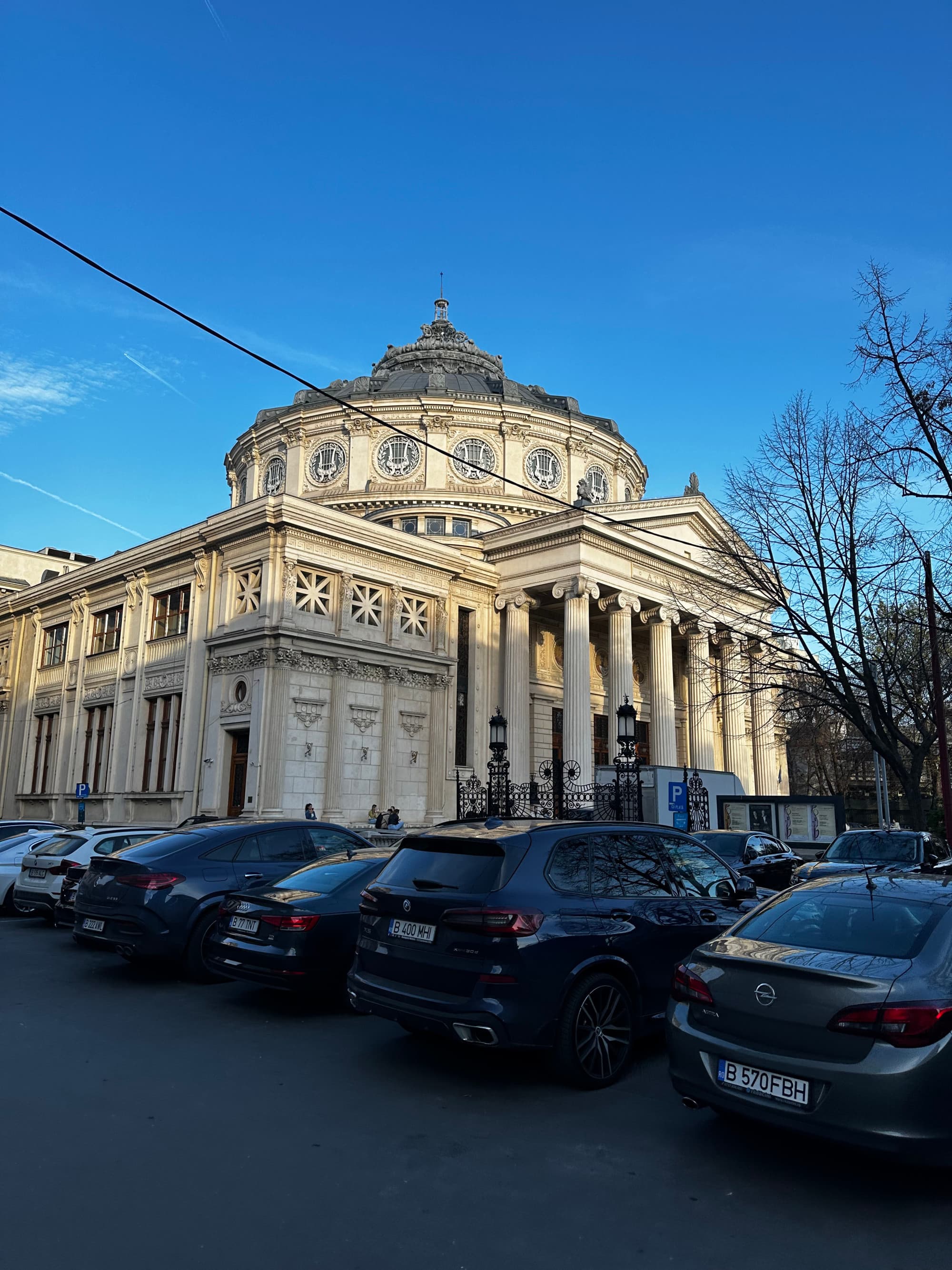 A picture of an old stone building with cars parked next to it and trees.