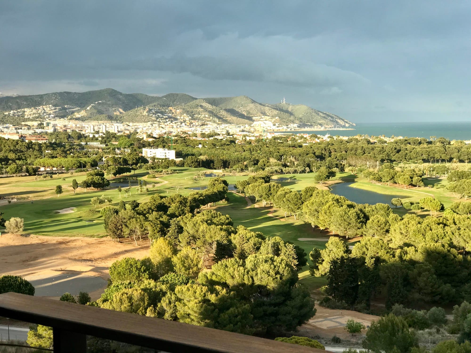 A view of a golf course with a city, sea and mountains in the background.