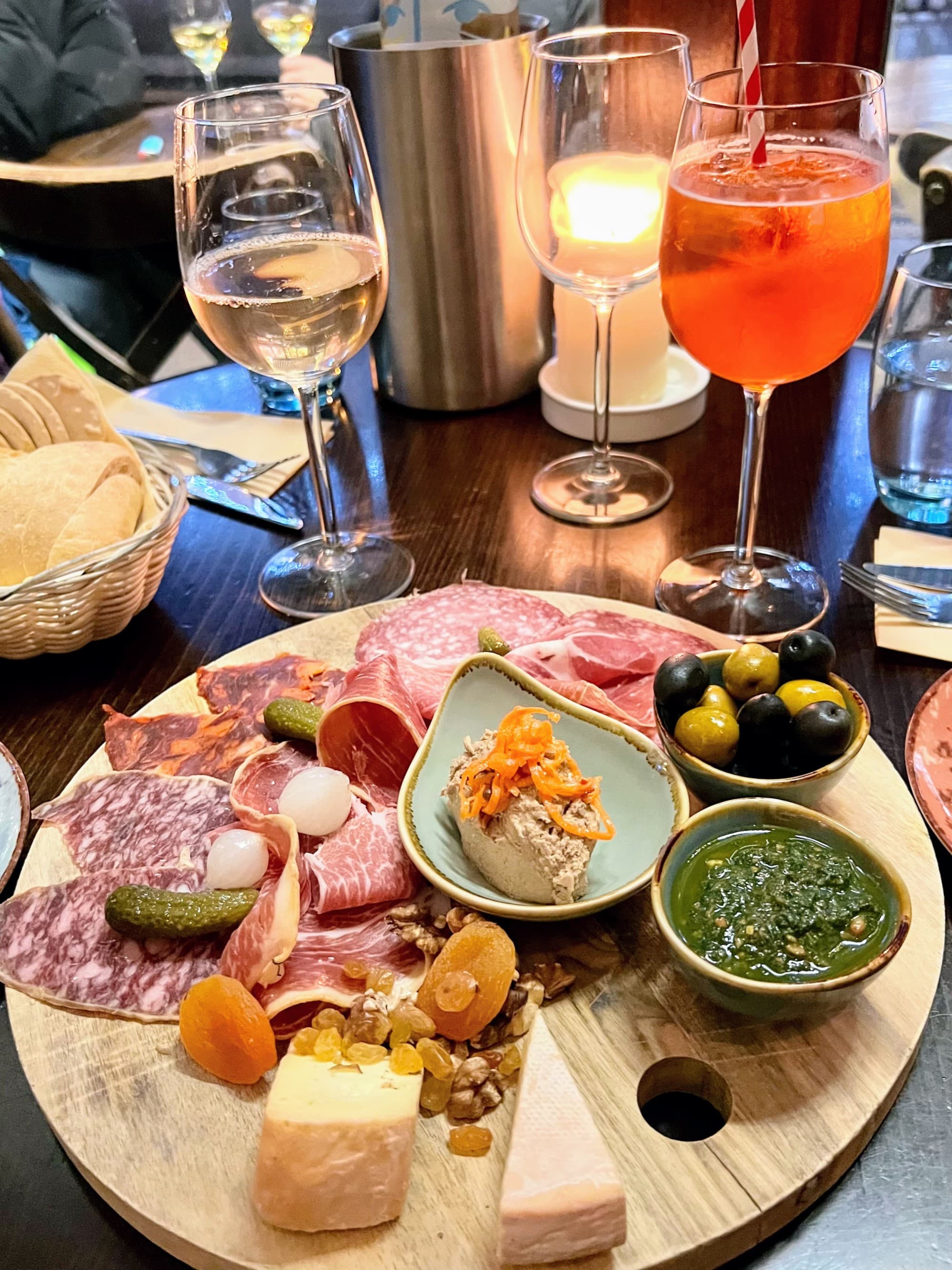 A charcuterie board on top of a table next to a glass of wine and Aperol Spritz.