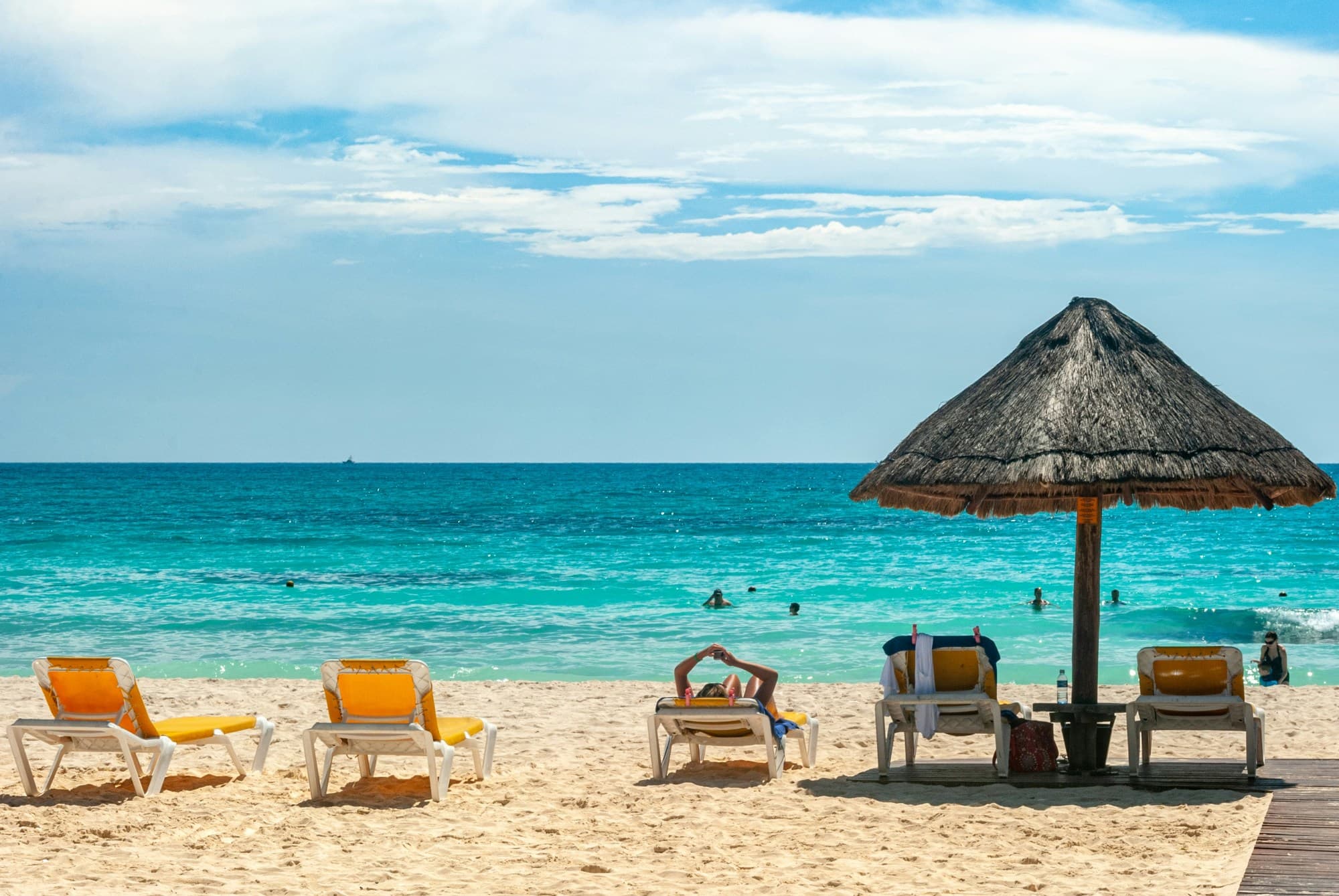 A beach with beach chairs and a thatched umbrella looking out at a turquoise ocean on a sunny day near the Cancun Mexico Grand Mayan Riviera Maya.