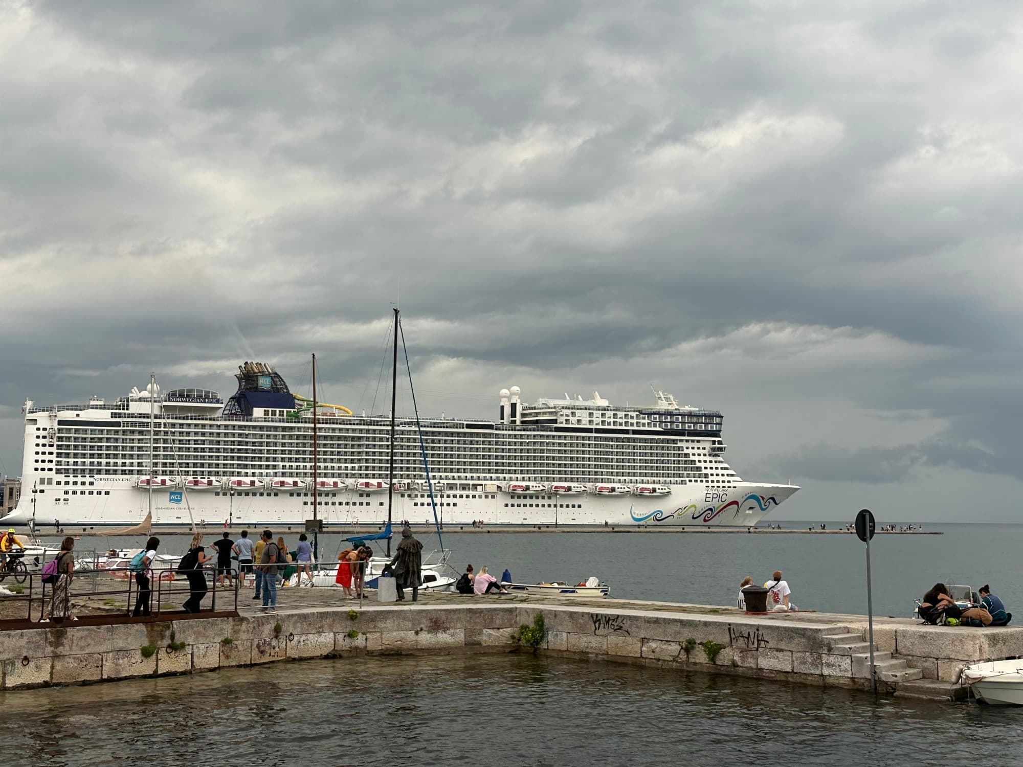 A cruise ship in a harbor with a line of people standing on a pier in front of it.