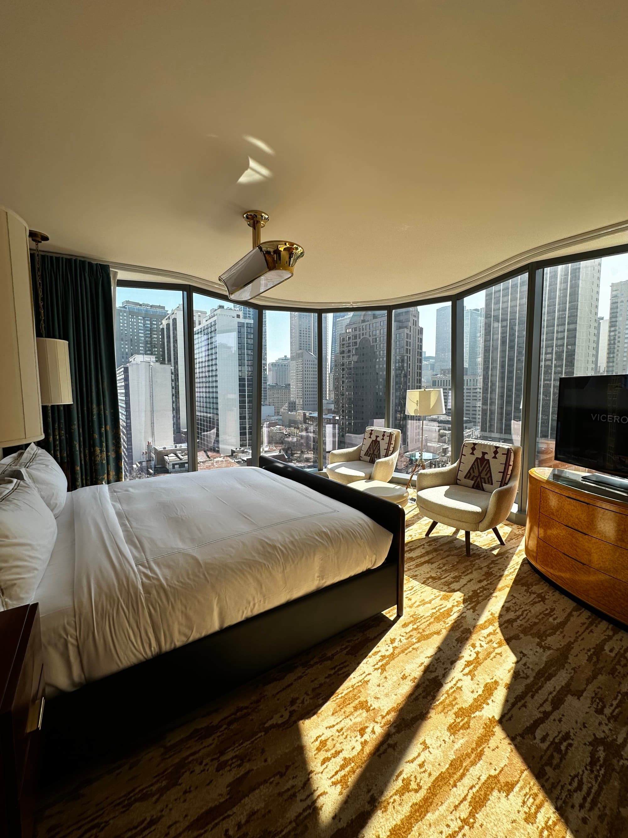 A hotel room with tall windows throughout giving a view of a city skyline