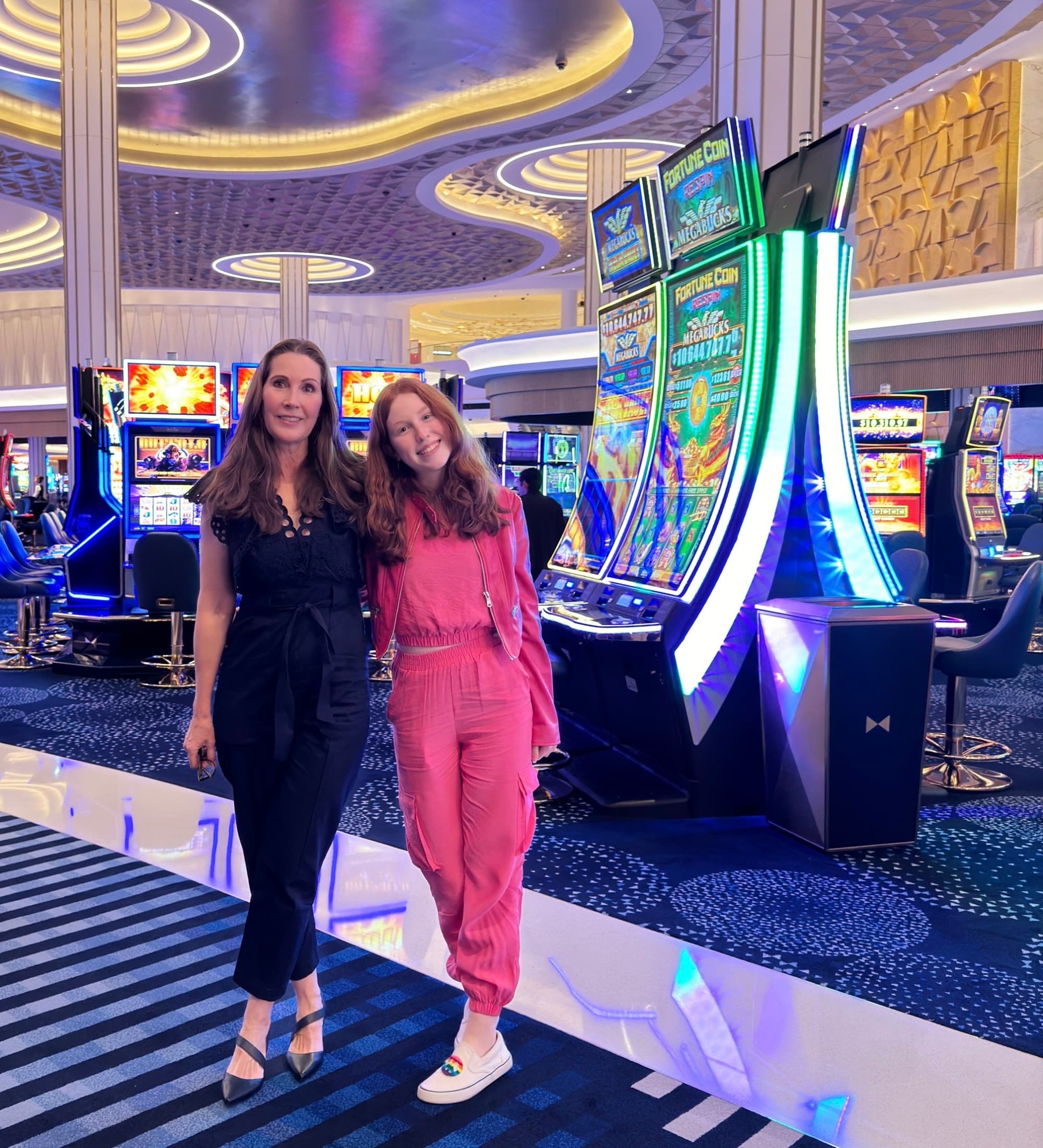 A woman in a black jumpsuit and a woman in a pink jumpsuit standing on a casino floor.