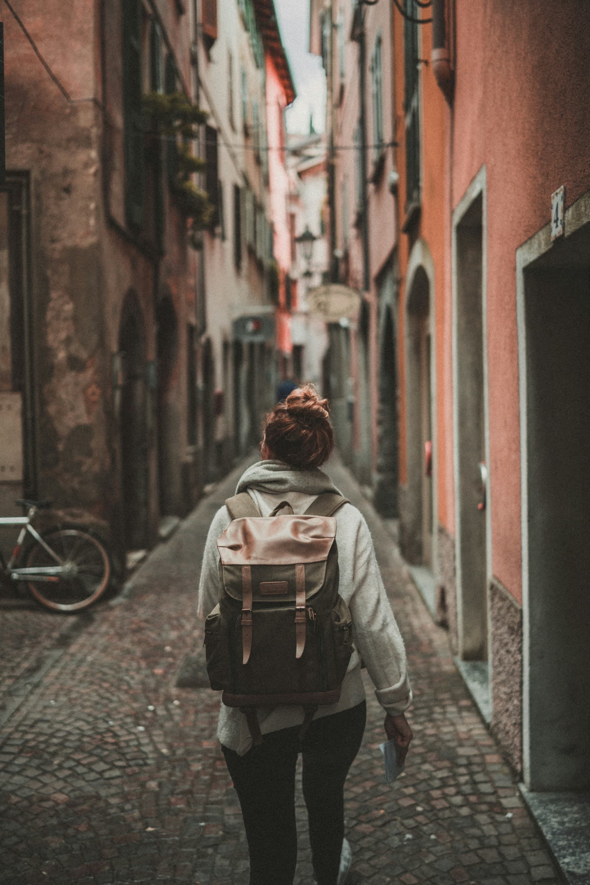 A person wearing a backpack walking down a narrow, cobblestone alley surrounded by colorful, European buildings.