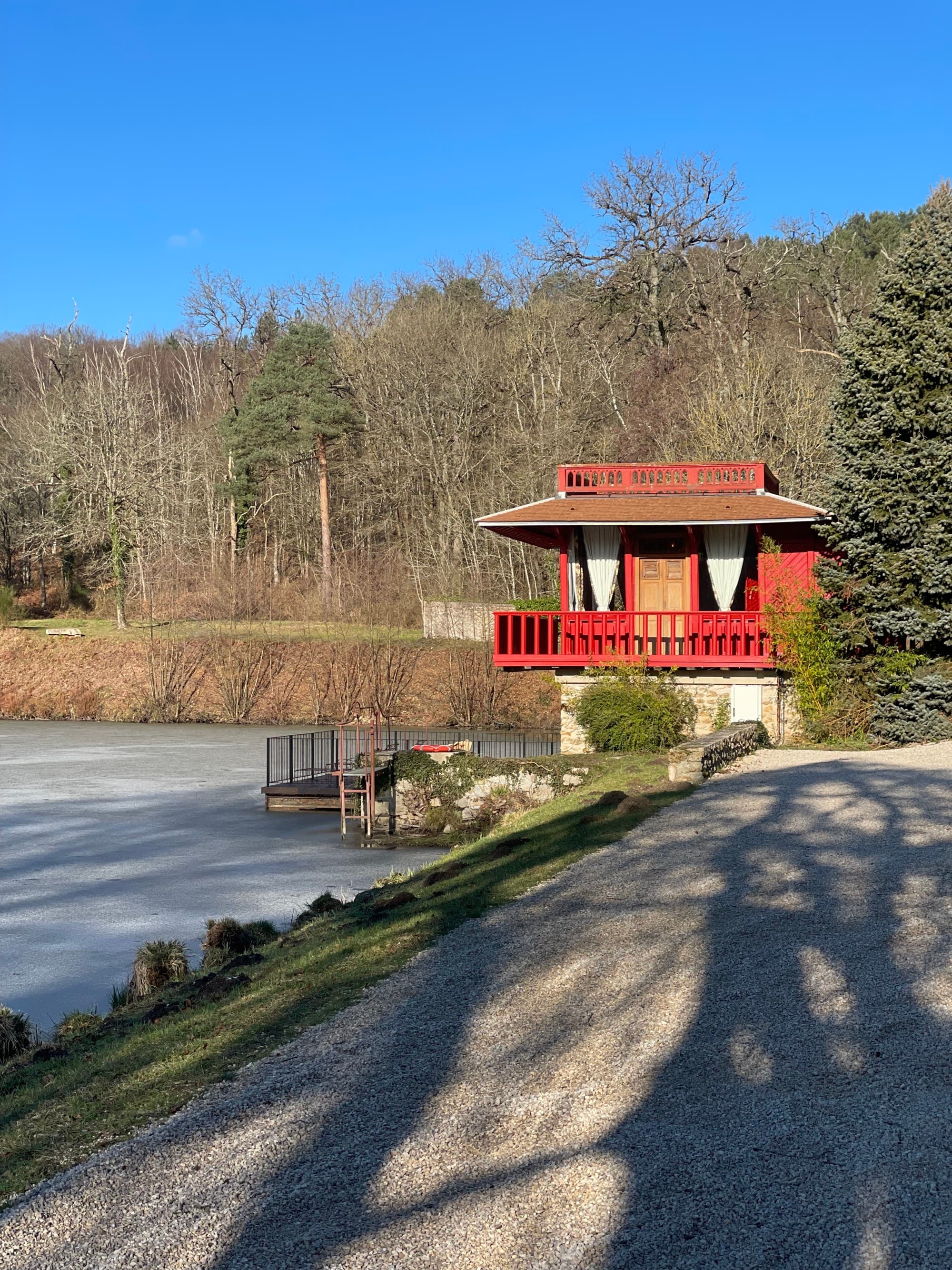 A red house in the distance with a concrete road, trees and frozen lake in the surrounding area.