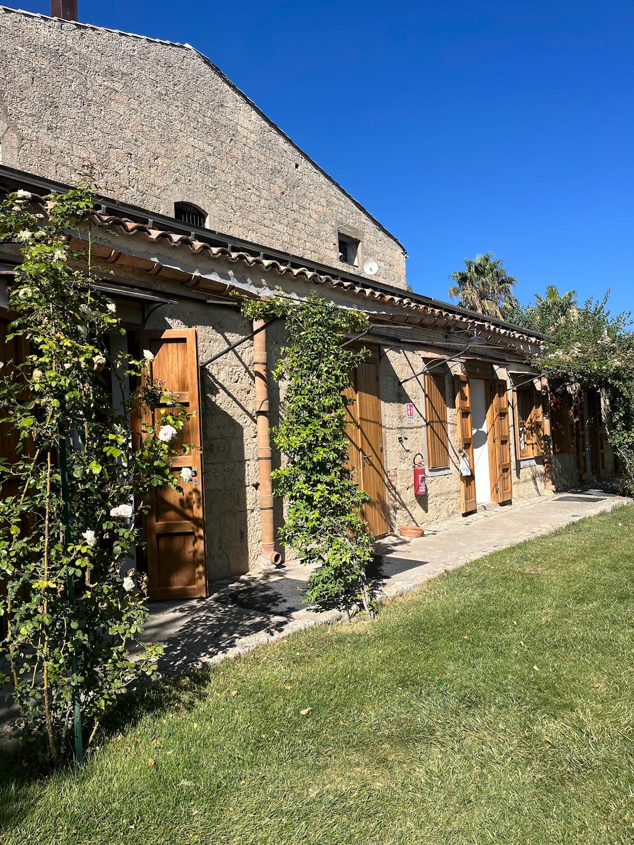 A grassy lawn in front of a stone building with a terrace that has wooden doors and lots of vines.