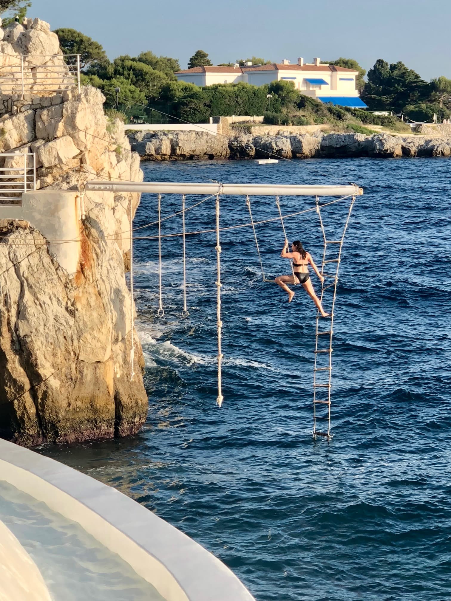 DuCapTrapeze - a woman in a black swimsuit on a ropes course over the sea that is attached to a rocky cliffside