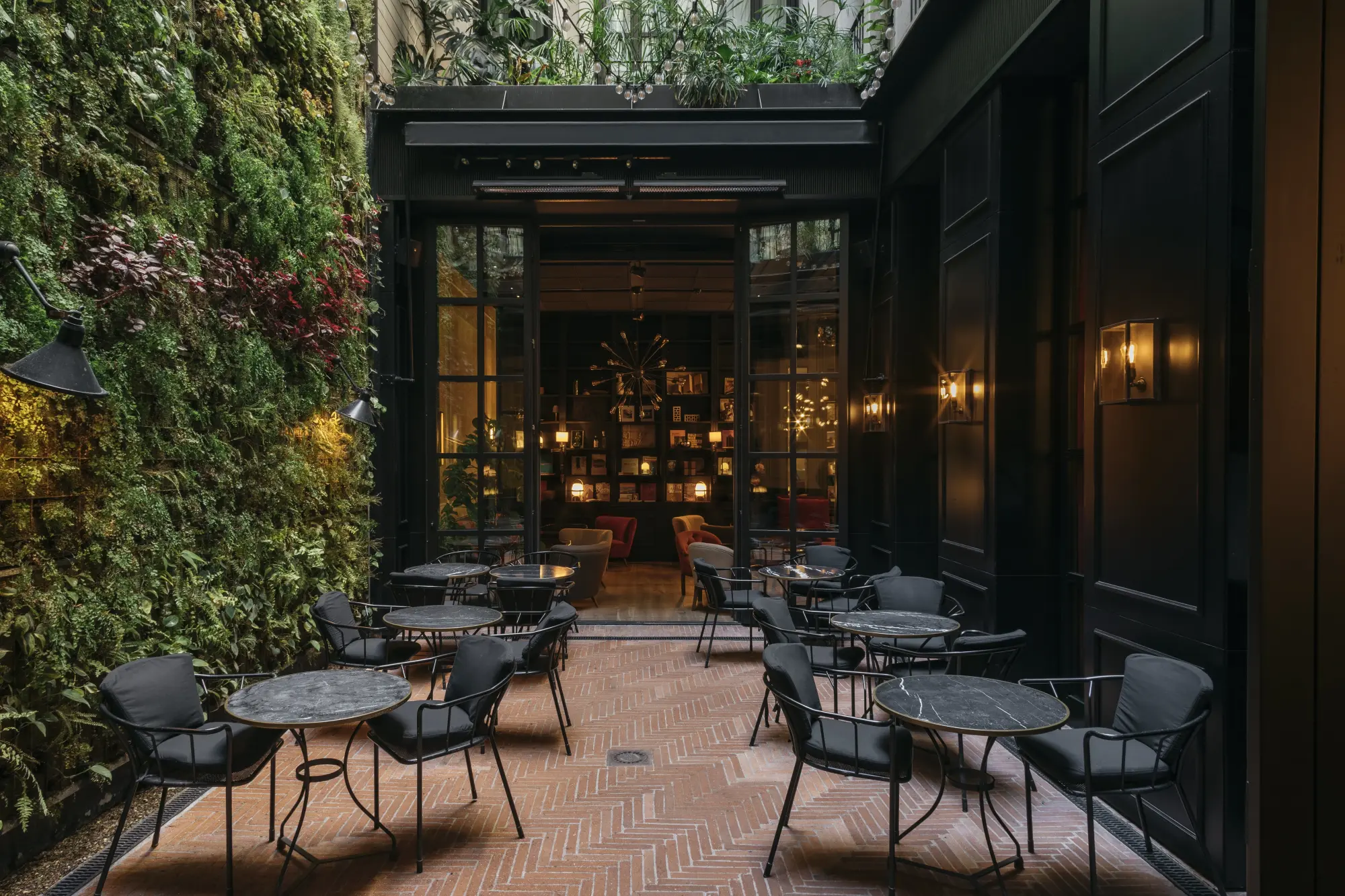 a luxe hotel courtyard with black metal tables and chairs and a plant wall