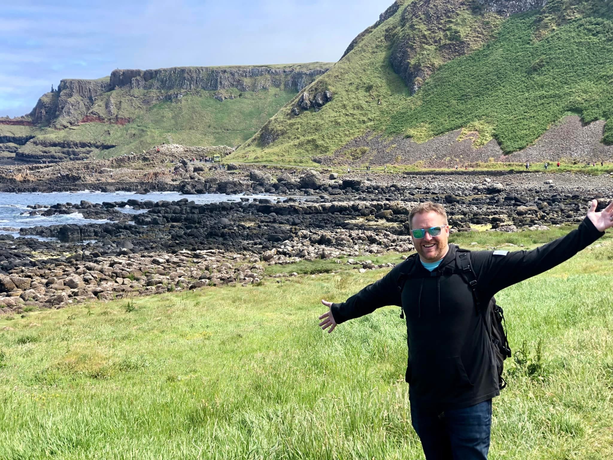 Travel advisor Michael in a black outfit standing at Giant's Causeway in a grassy meadow with hills in view
