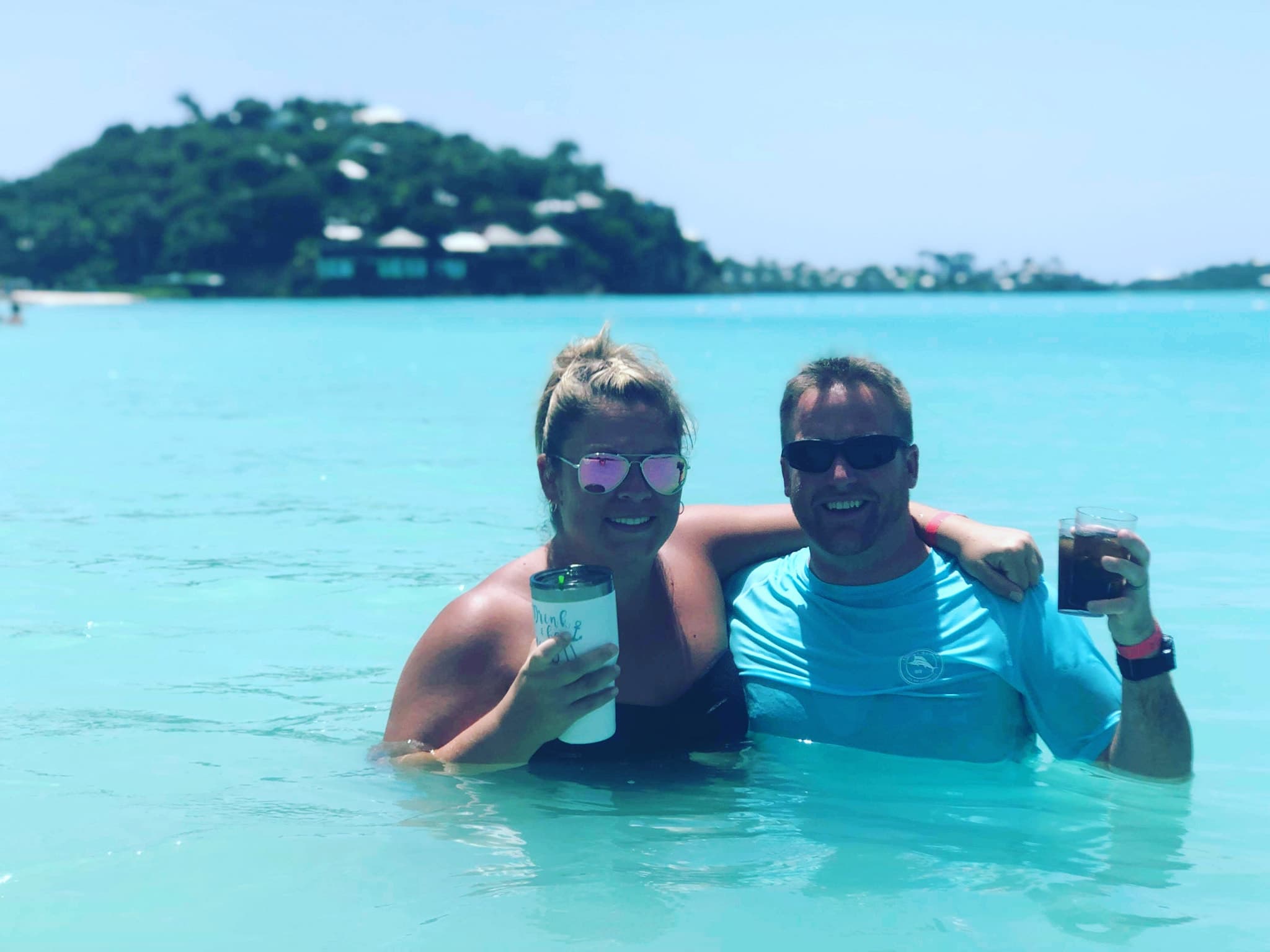 Picture of Michael in a blue shirt holding a drink with female companion in the ocean