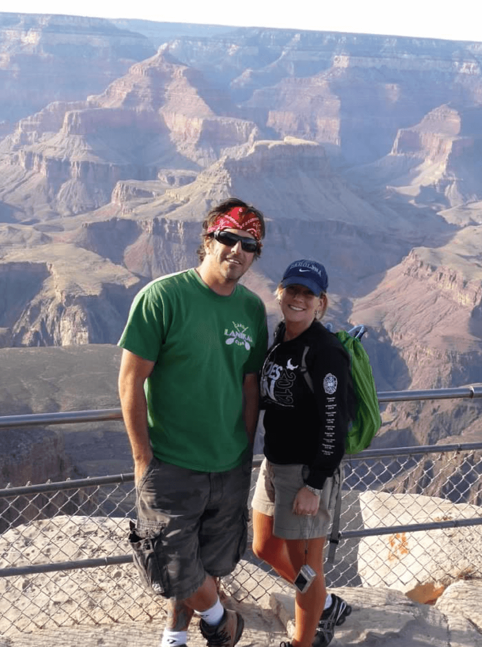 Shannon and a man posing in front of a fence with the Grand Canyon in the background.