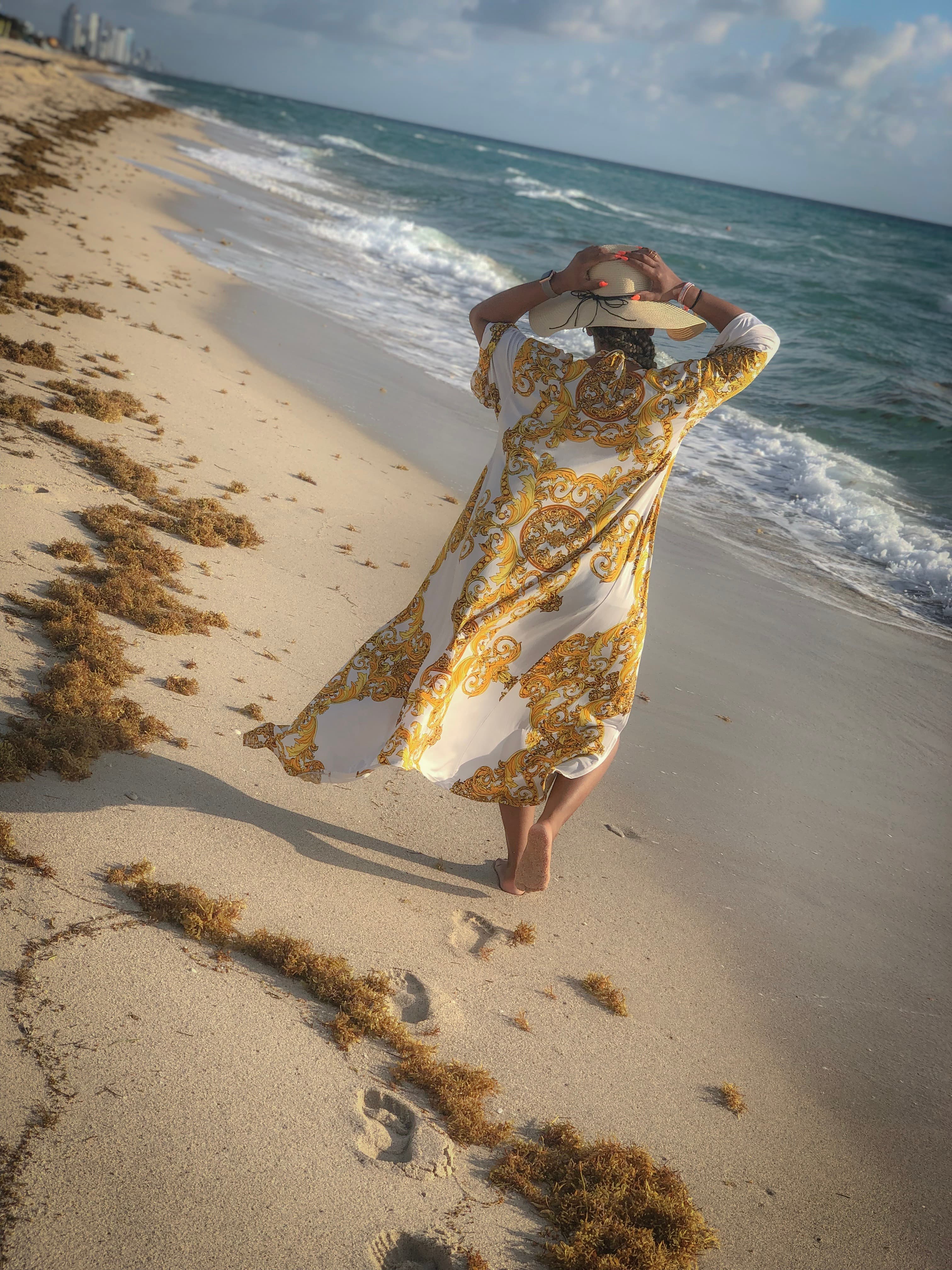 Travel advisor Libby walking on the beach in a white and yellow dress and hut