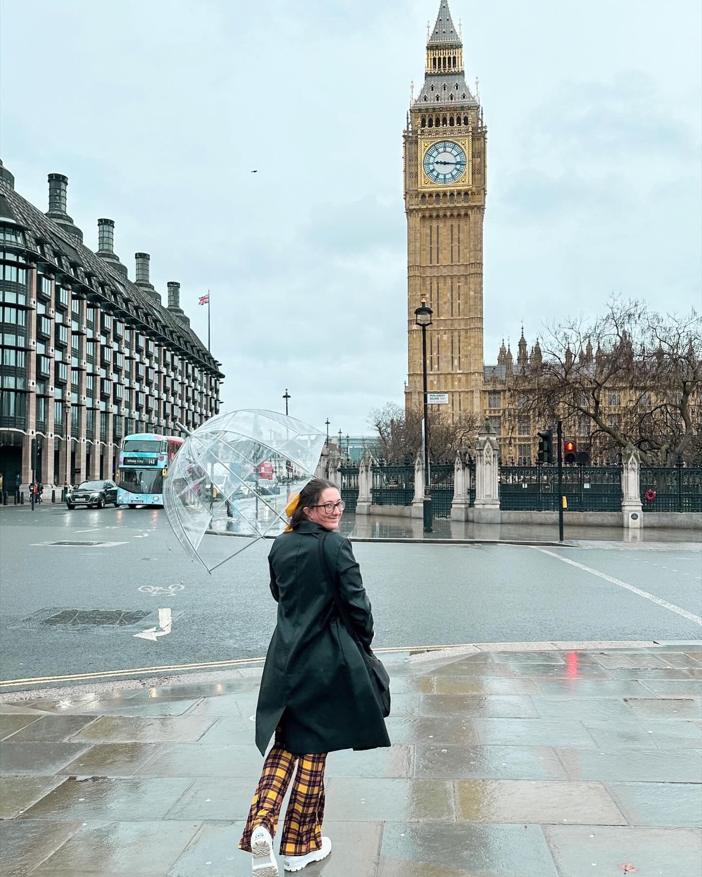 Travel advisor Tessa holding an umbrella with a London street and Big Ben in view on a cloudy day.