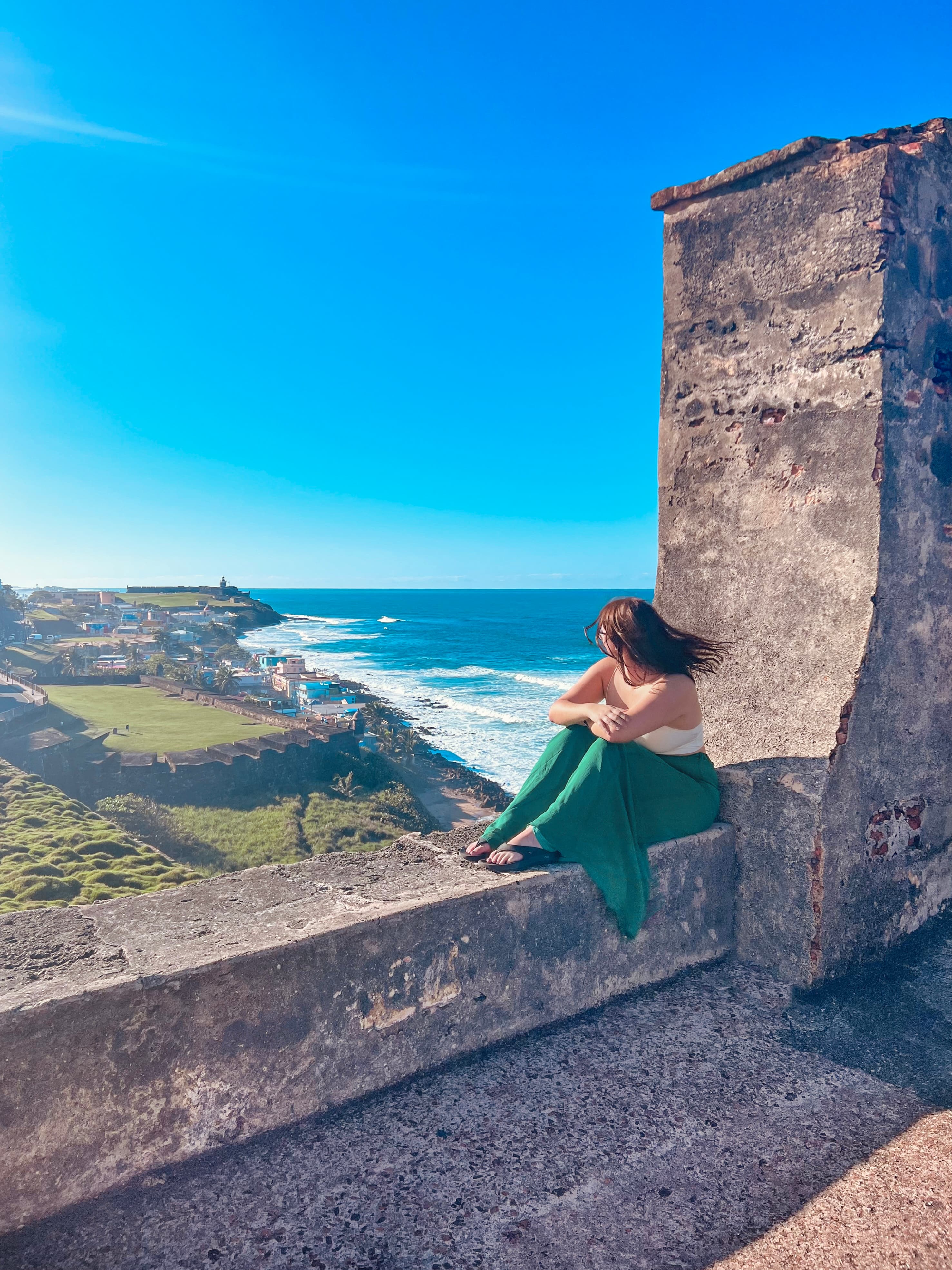 Travel advisor Tessa sitting on a stone wall overlooking a beautiful view of green landsacpe and ocean