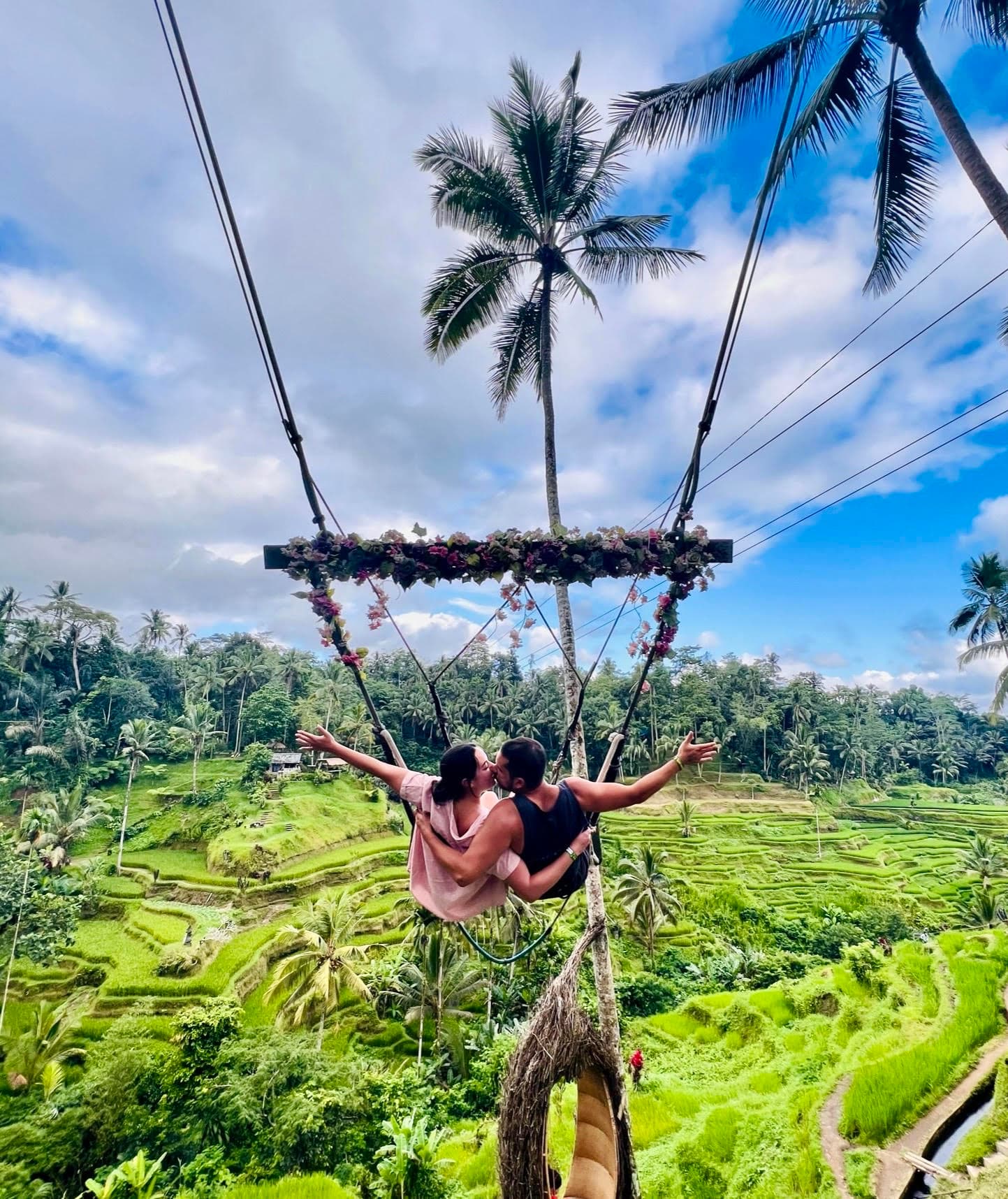 Travel advisor Cortney posing on a swing kissing male companion high above a lush forest