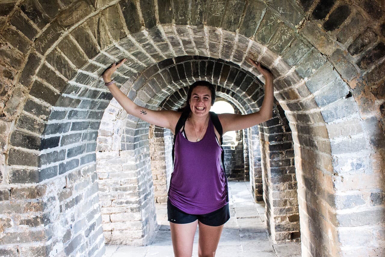 Travel advisor Rachel in a purple shirt and black shorts posing inside a tunnel-shaped wall structure in the Mutianyu Great Wall